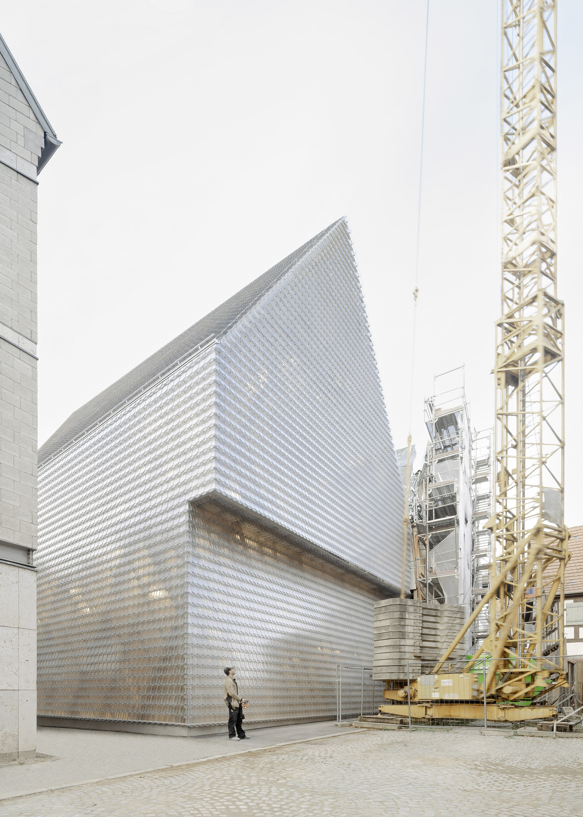 Street view showing the gabled glass brick facade beside a yellow construction crane