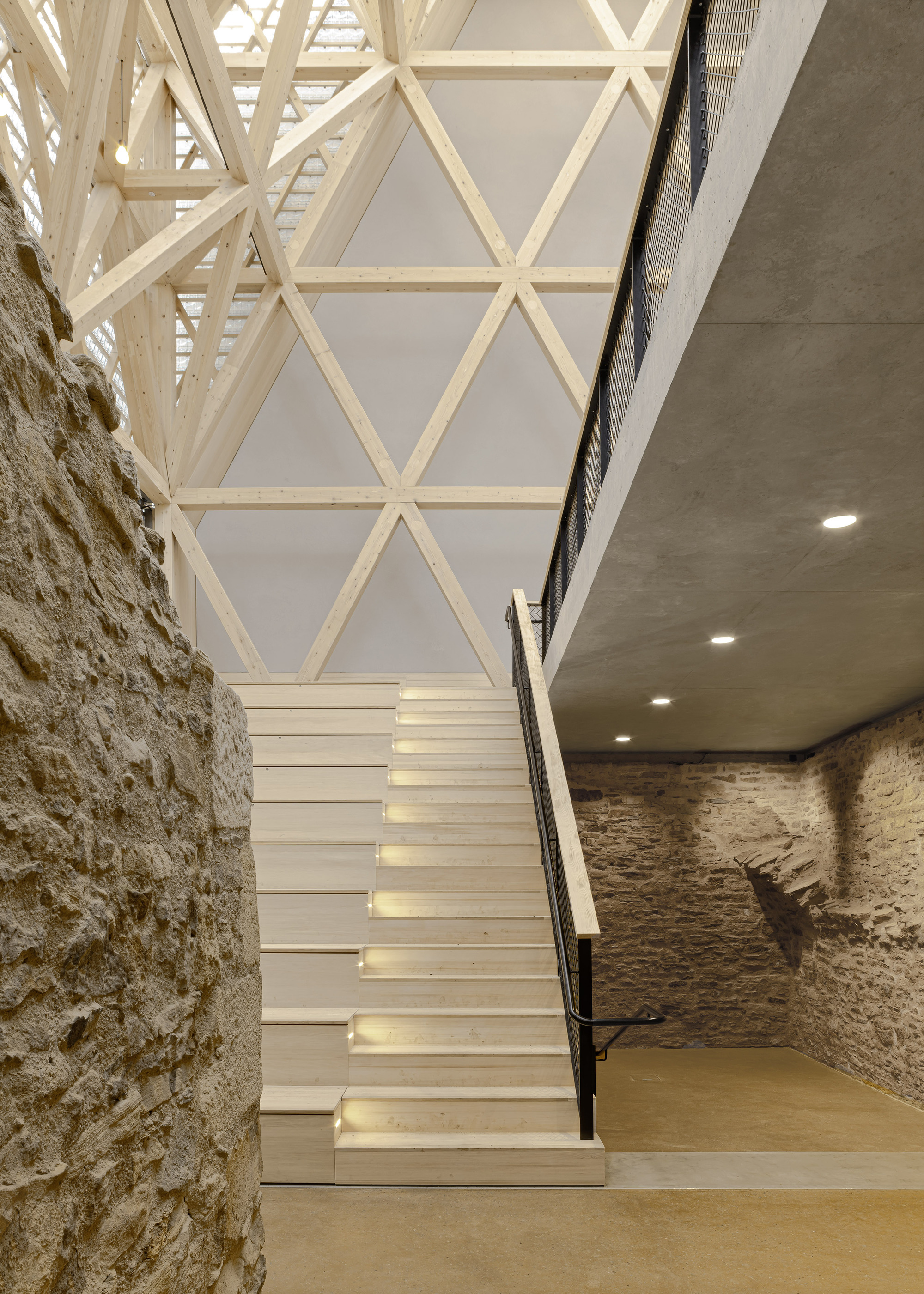 White painted staircase ascending between exposed stone wall and triangulated timber roof framework