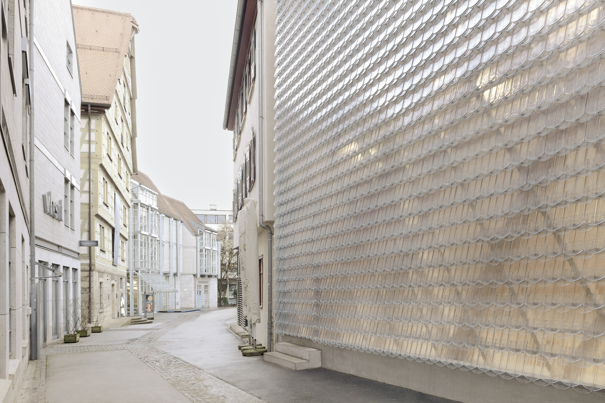 Narrow cobbled street with the textured glass brick wall rising alongside residential buildings