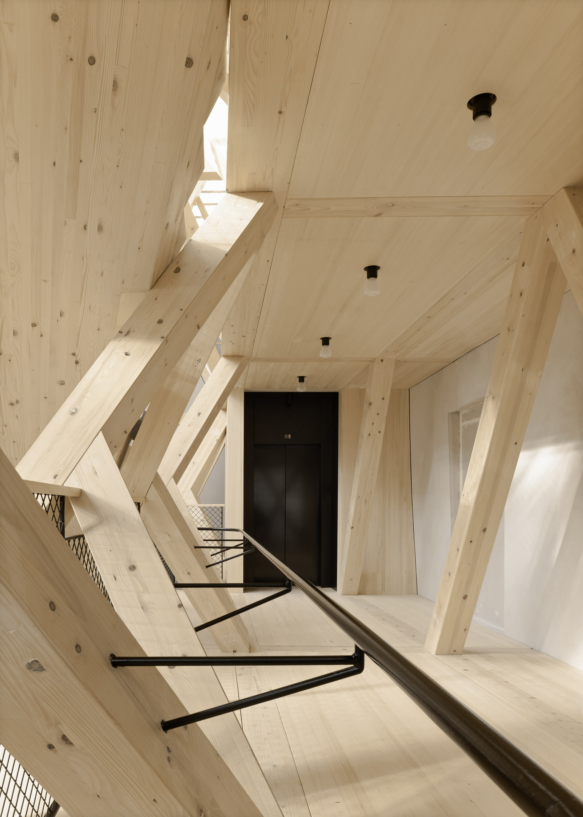 Upward view along the timber-clad stairwell with a black elevator door at the landing