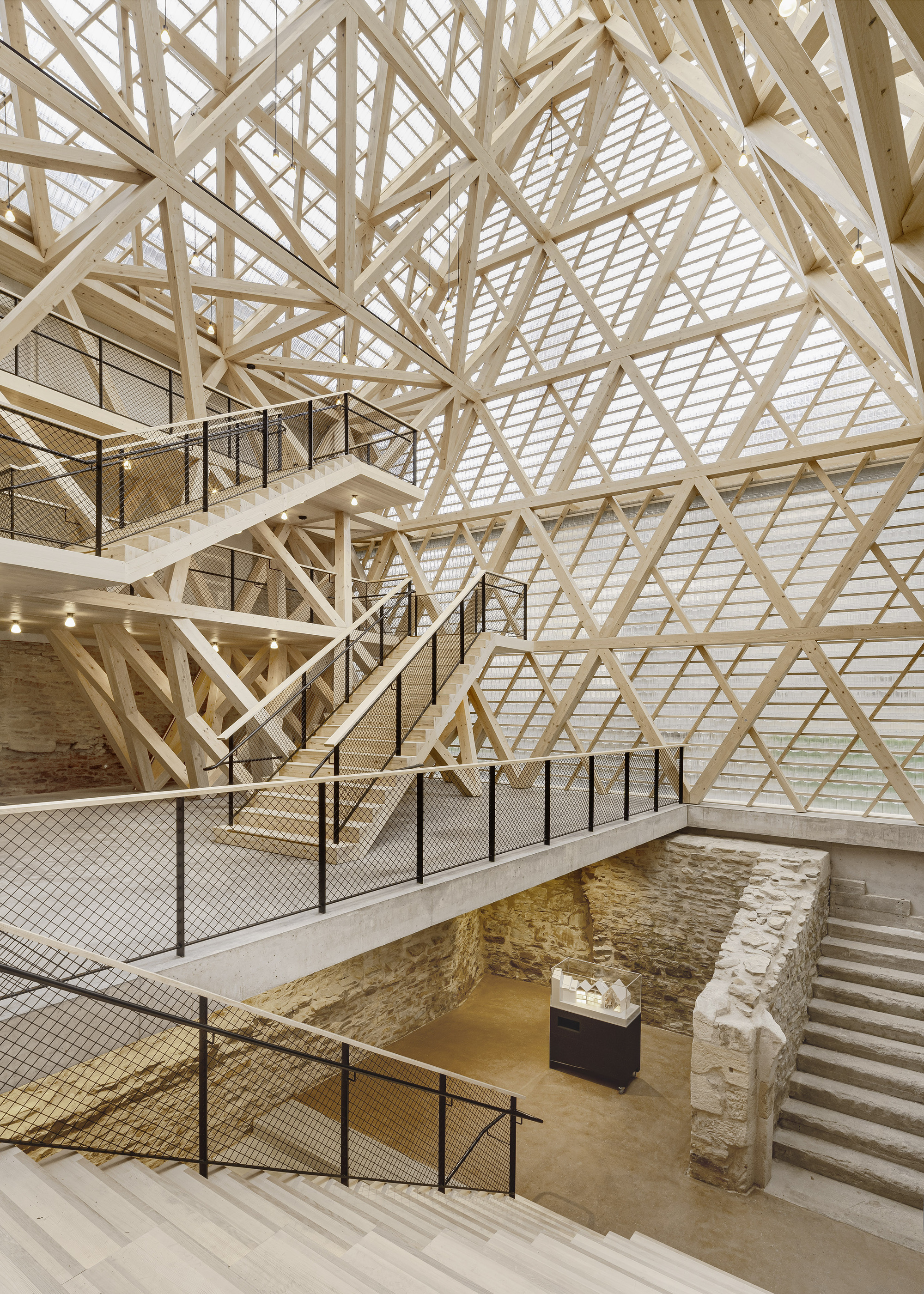 Multi-level interior showing crisscrossing staircases and exposed stone foundation walls beneath the timber lattice