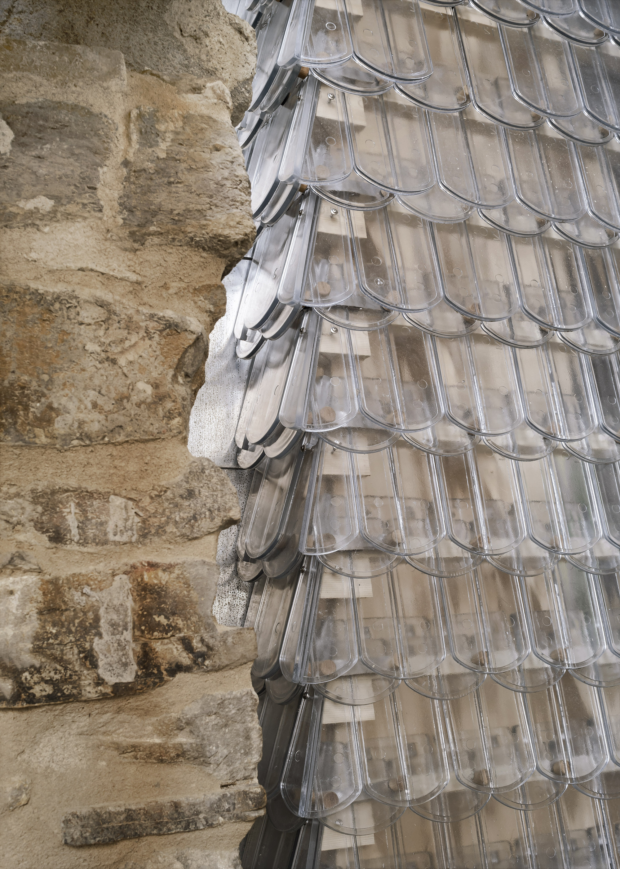 Detail of the translucent glass shingle facade meeting the excavated stone foundation wall