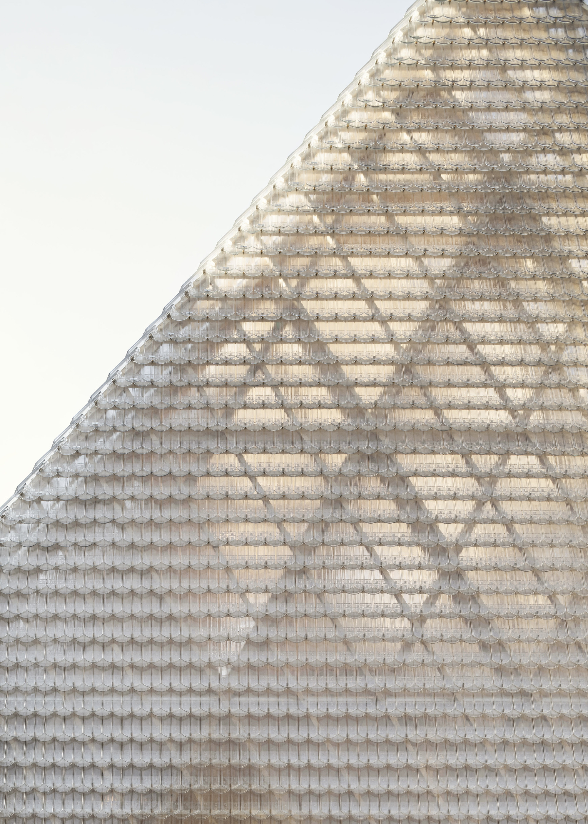Close-up of the textured glass tile roof surface rising toward a peaked ridge against an overcast sky