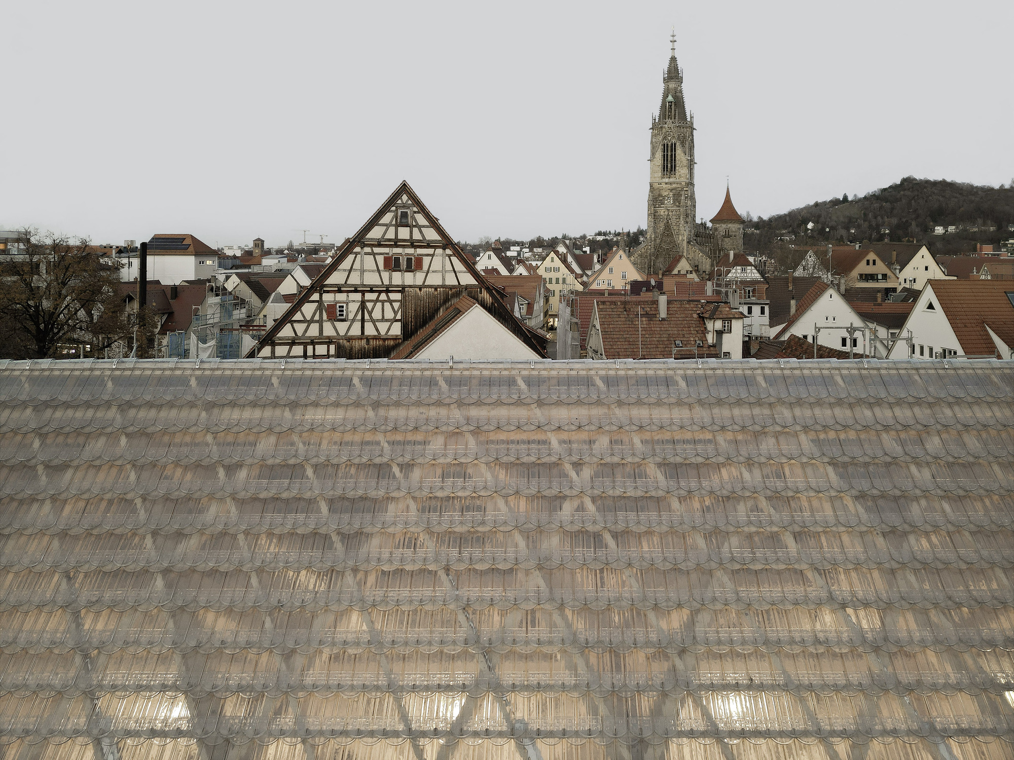 Sloped glass tile roof in the foreground with timber-framed buildings and a church spire beyond