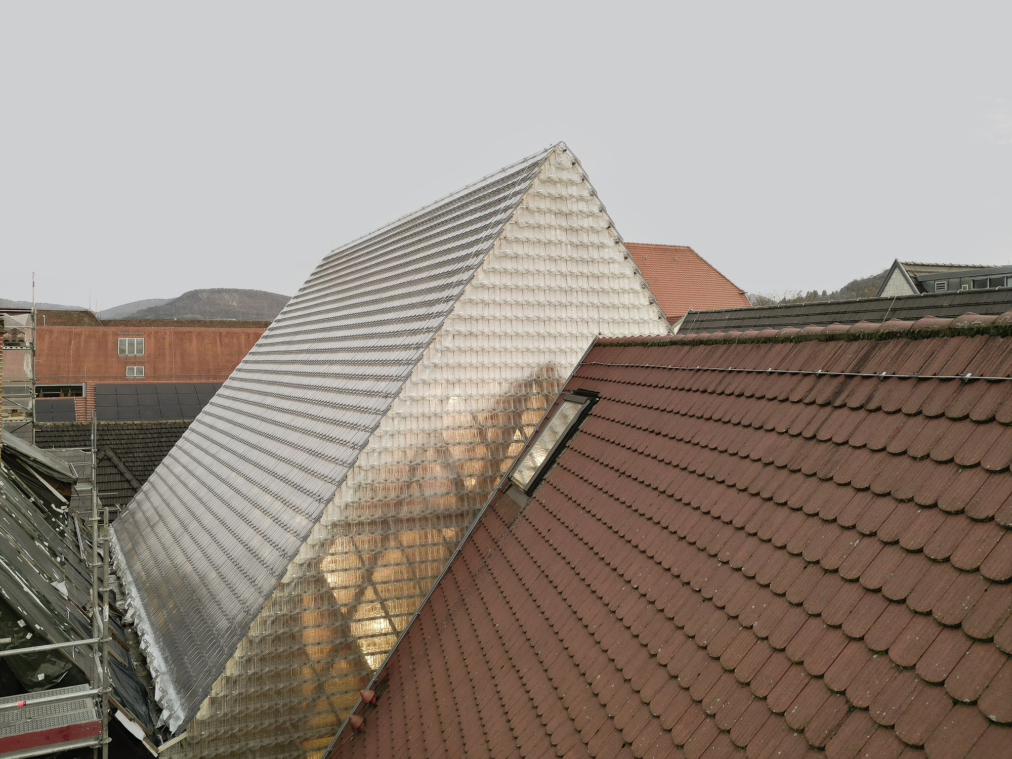 Pyramidal glass tile roof rising above surrounding red clay tile rooftops on an overcast day