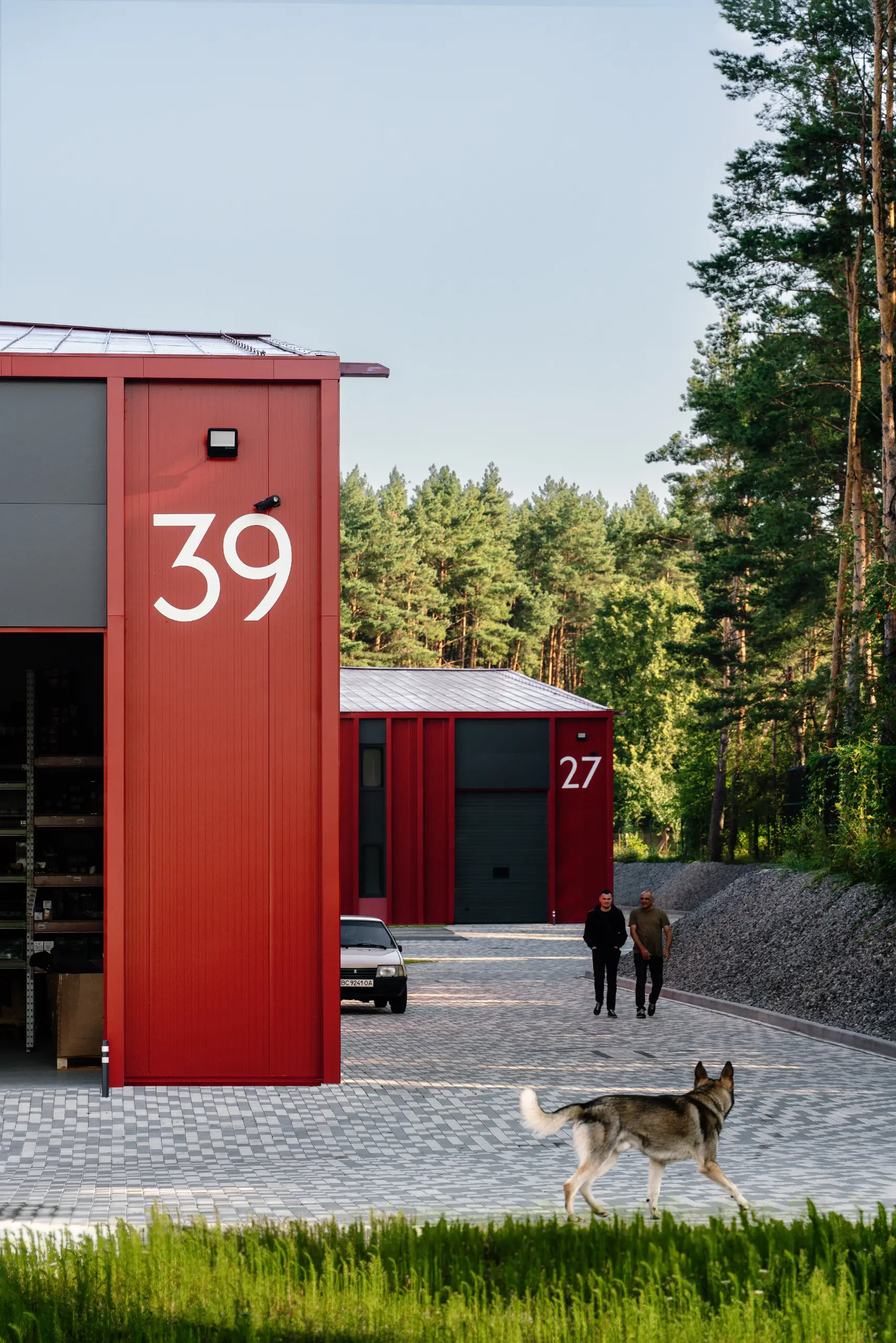 View of numbered red metal-clad units with a dog and people in a forested courtyard