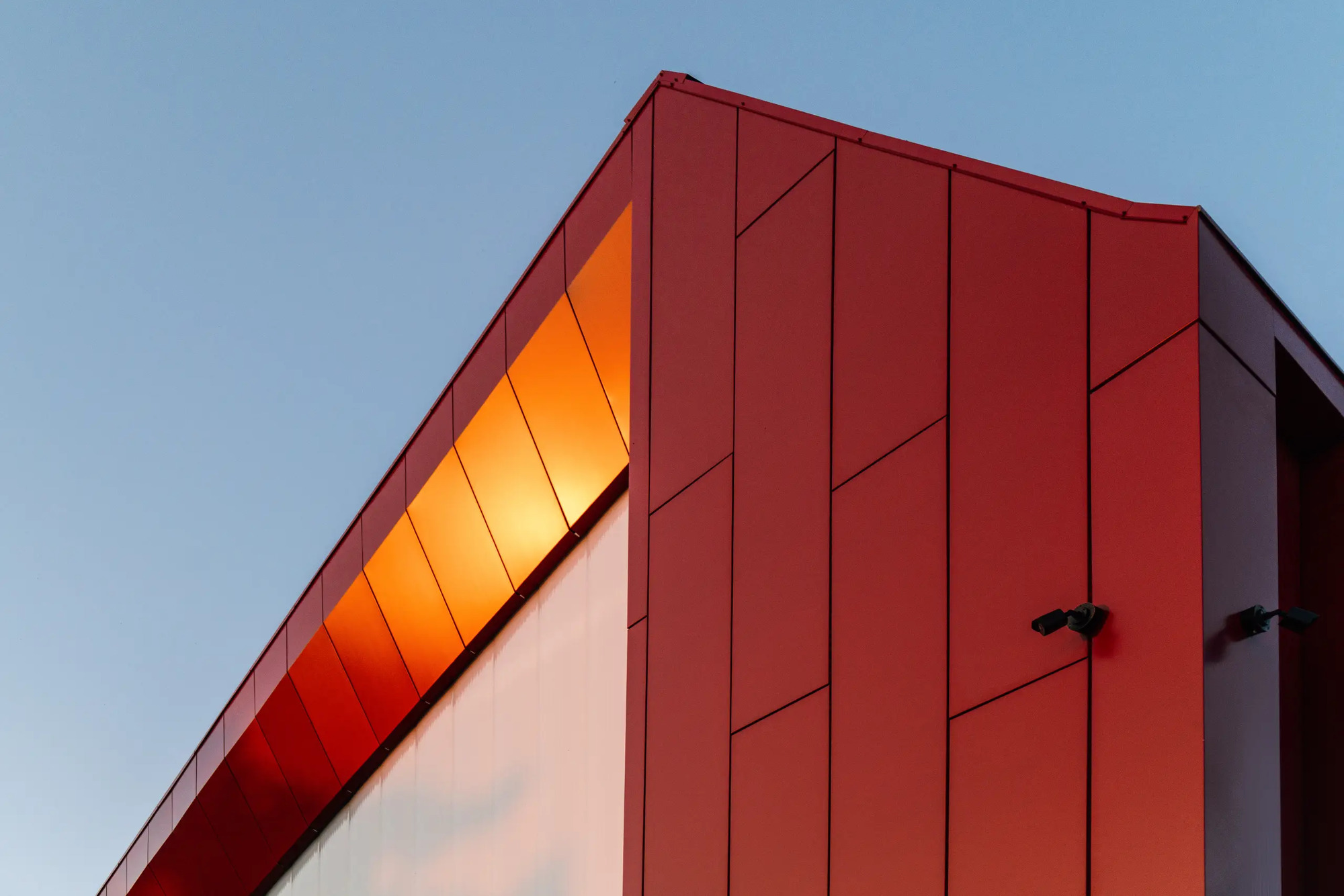 Upward view of the angled red metal panel soffit meeting the white wall at dusk
