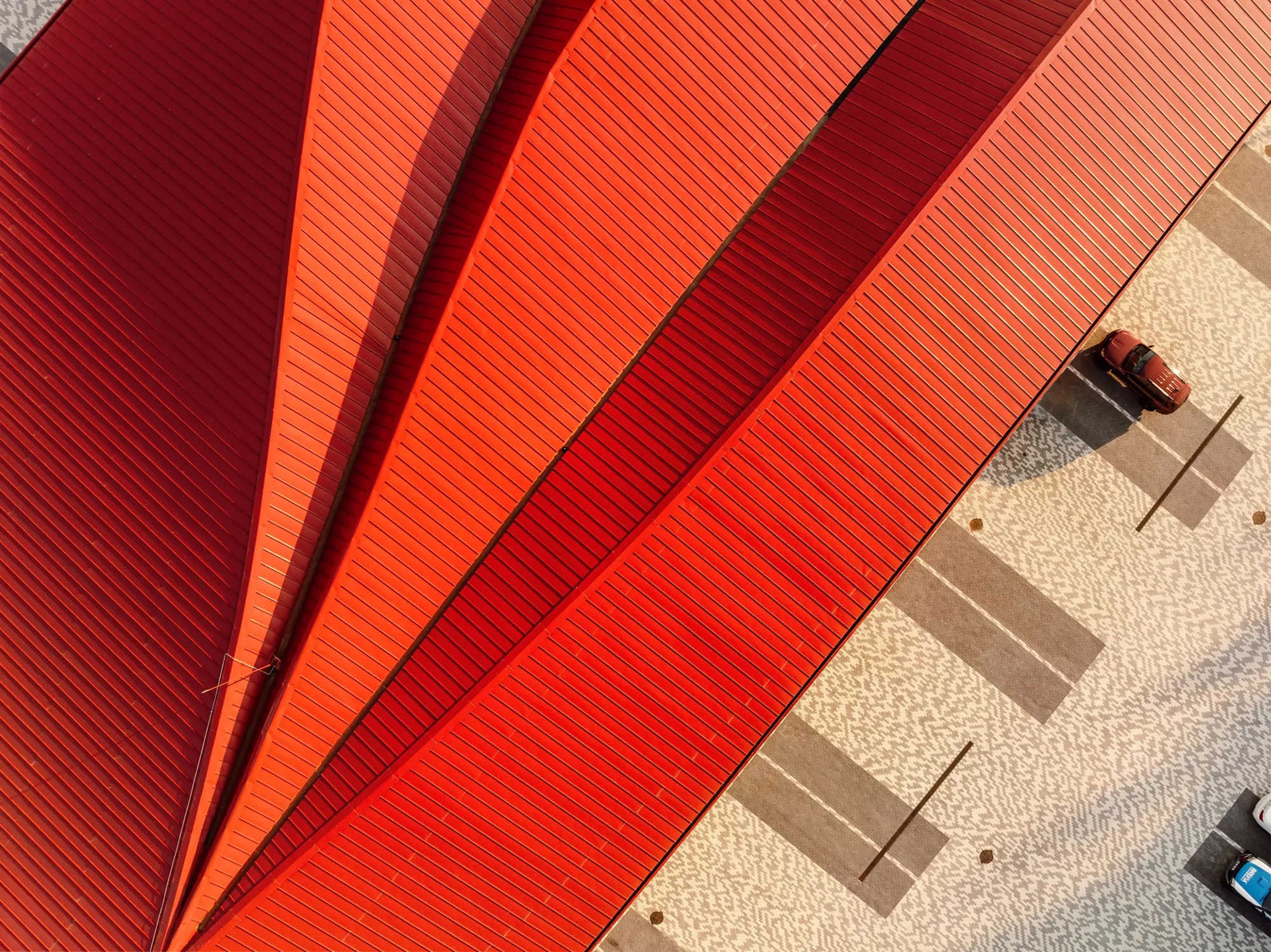 Aerial view of the radiating red metal roofs with parked cars casting shadows on the pavement