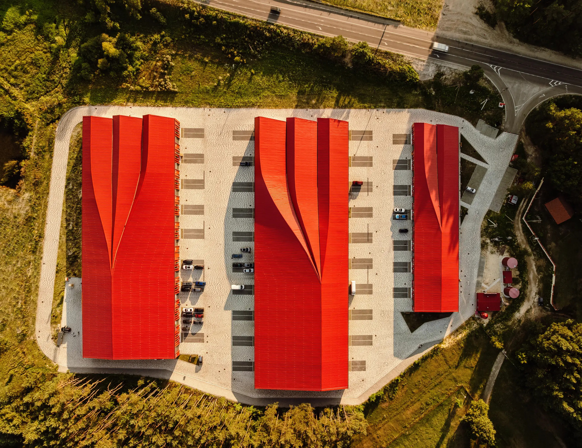 Drone view of three red corrugated roofs separated by parking bays and surrounded by forest