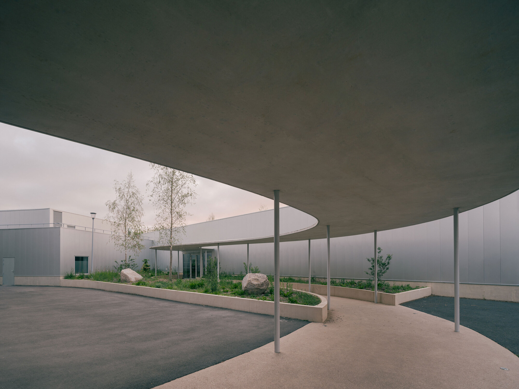 Circular canopy supported by slender columns sheltering a planted courtyard under overcast skies