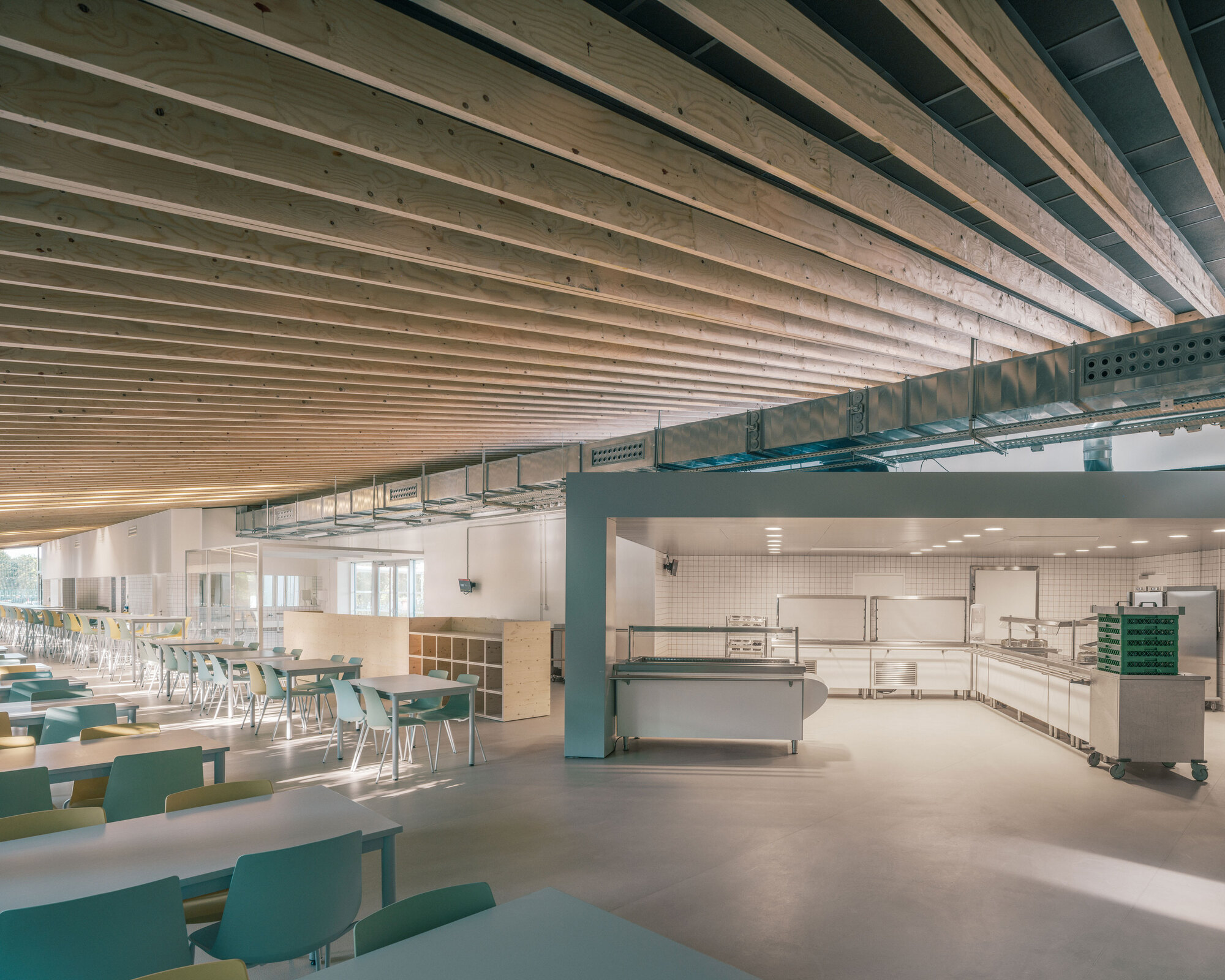 Exposed timber ceiling joists above cafeteria seating area and service counter with mechanical ducting