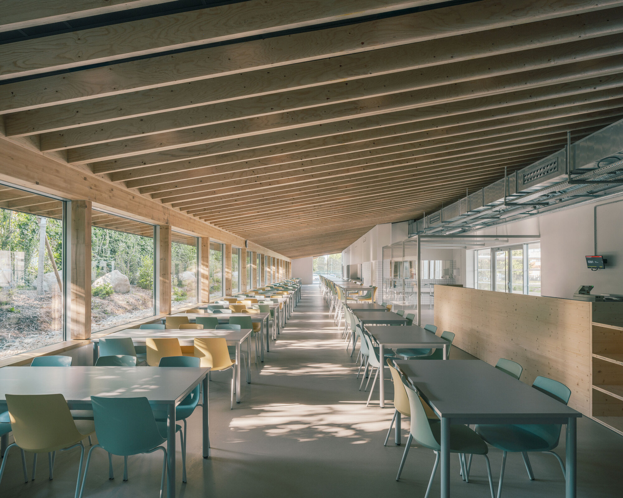 Dining hall interior with timber ceiling joists and rows of tables along glazed walls