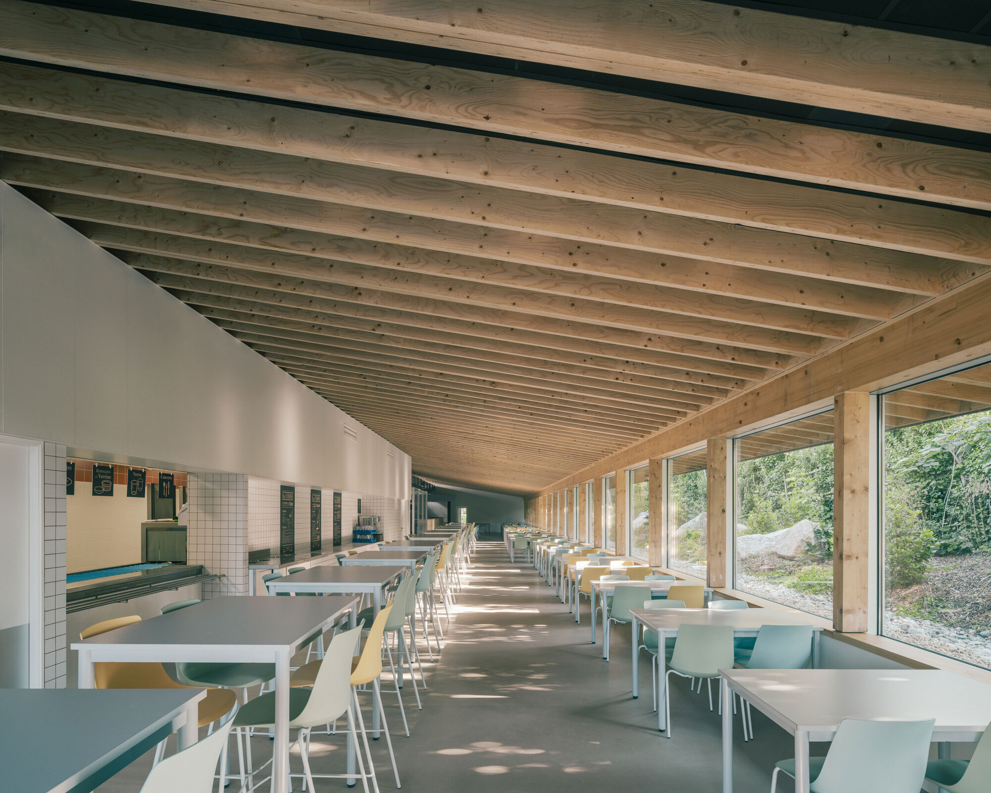 Canteen with parallel rows of tables under rhythmic timber beams and continuous glazing