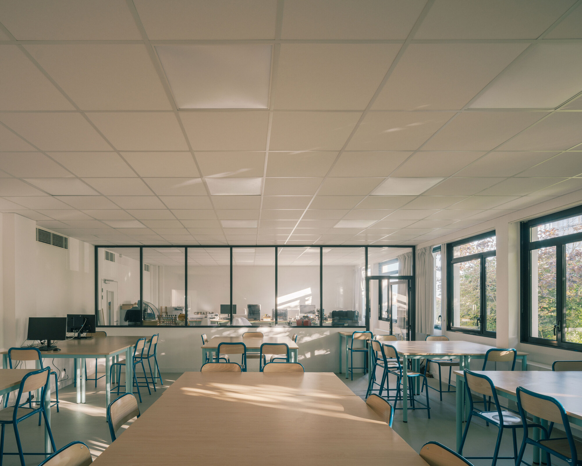 Classroom with suspended acoustic ceiling tiles and glazed partition to adjacent spaces in afternoon light