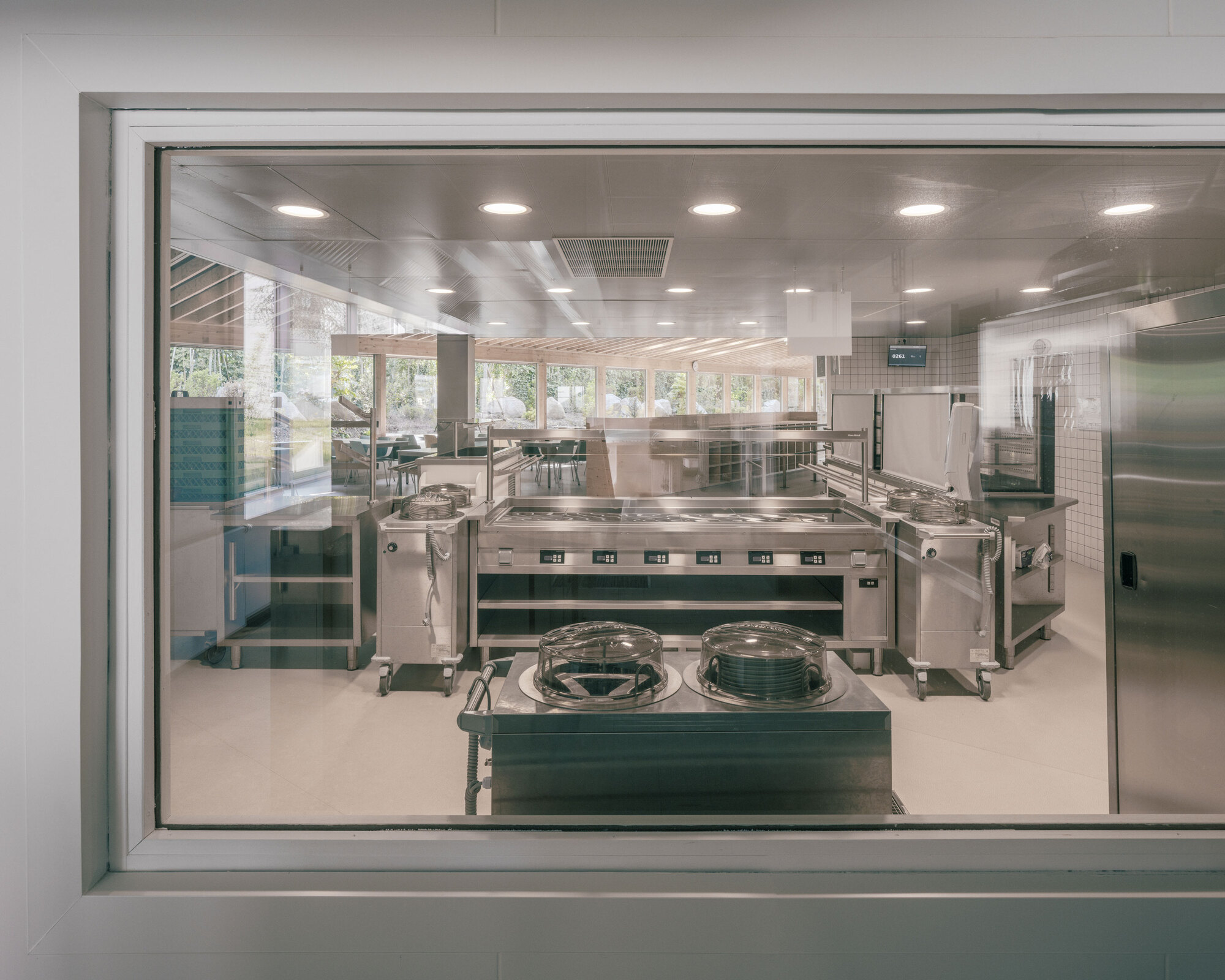 View through serving window into the stainless steel commercial kitchen with equipment islands