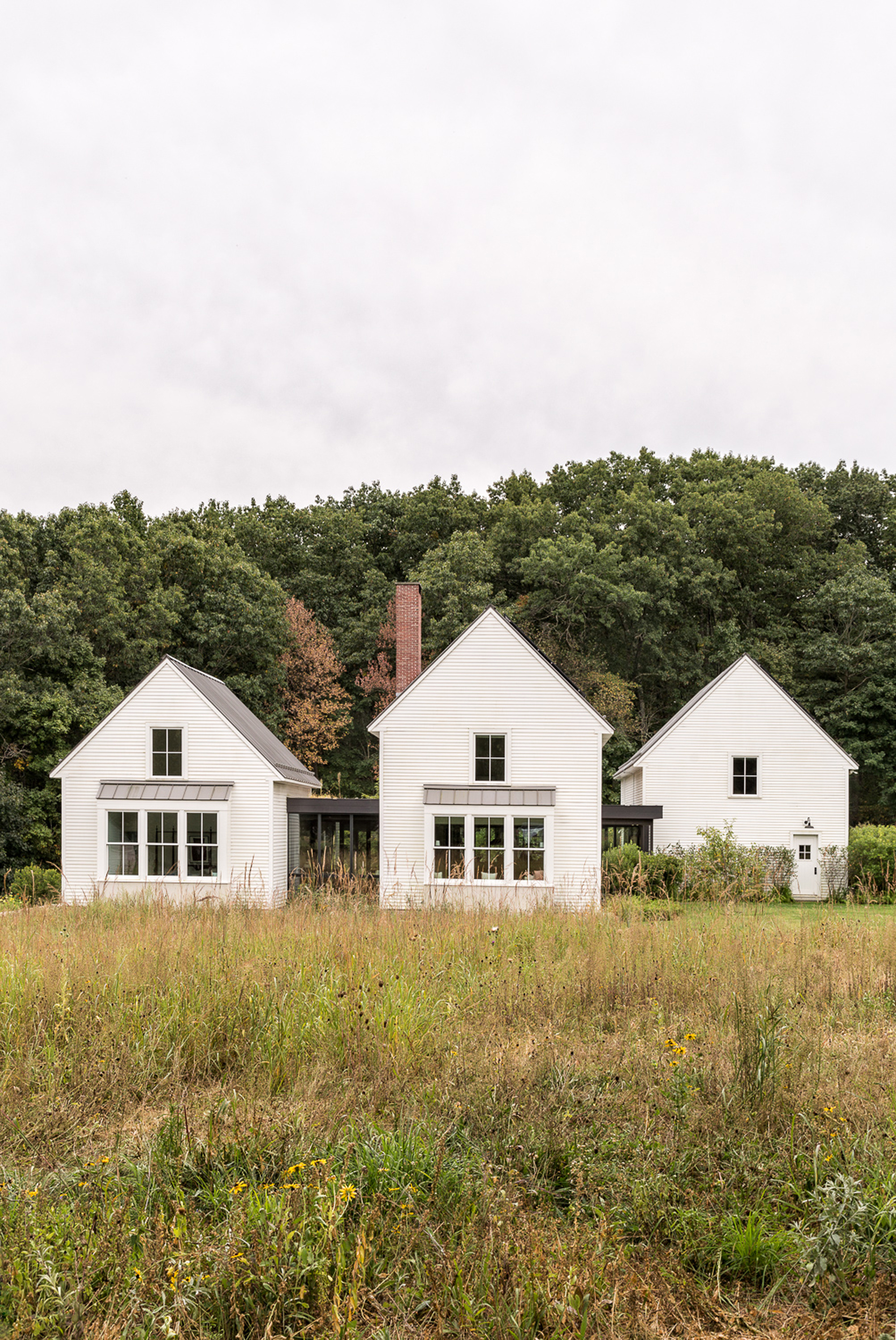 Rear elevation of three connected gabled structures with horizontal siding and brick chimney