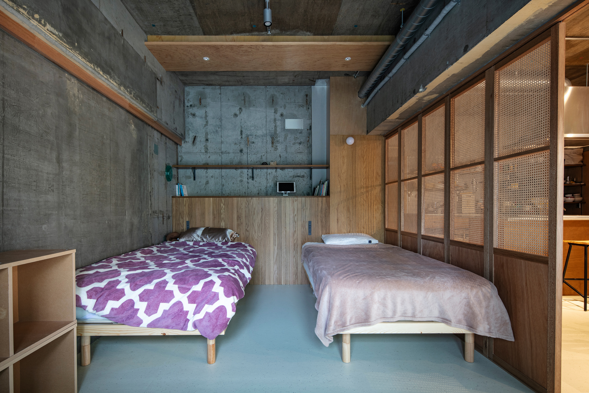 Bedroom with two platform beds on pale green flooring and cane sliding partitions along concrete walls