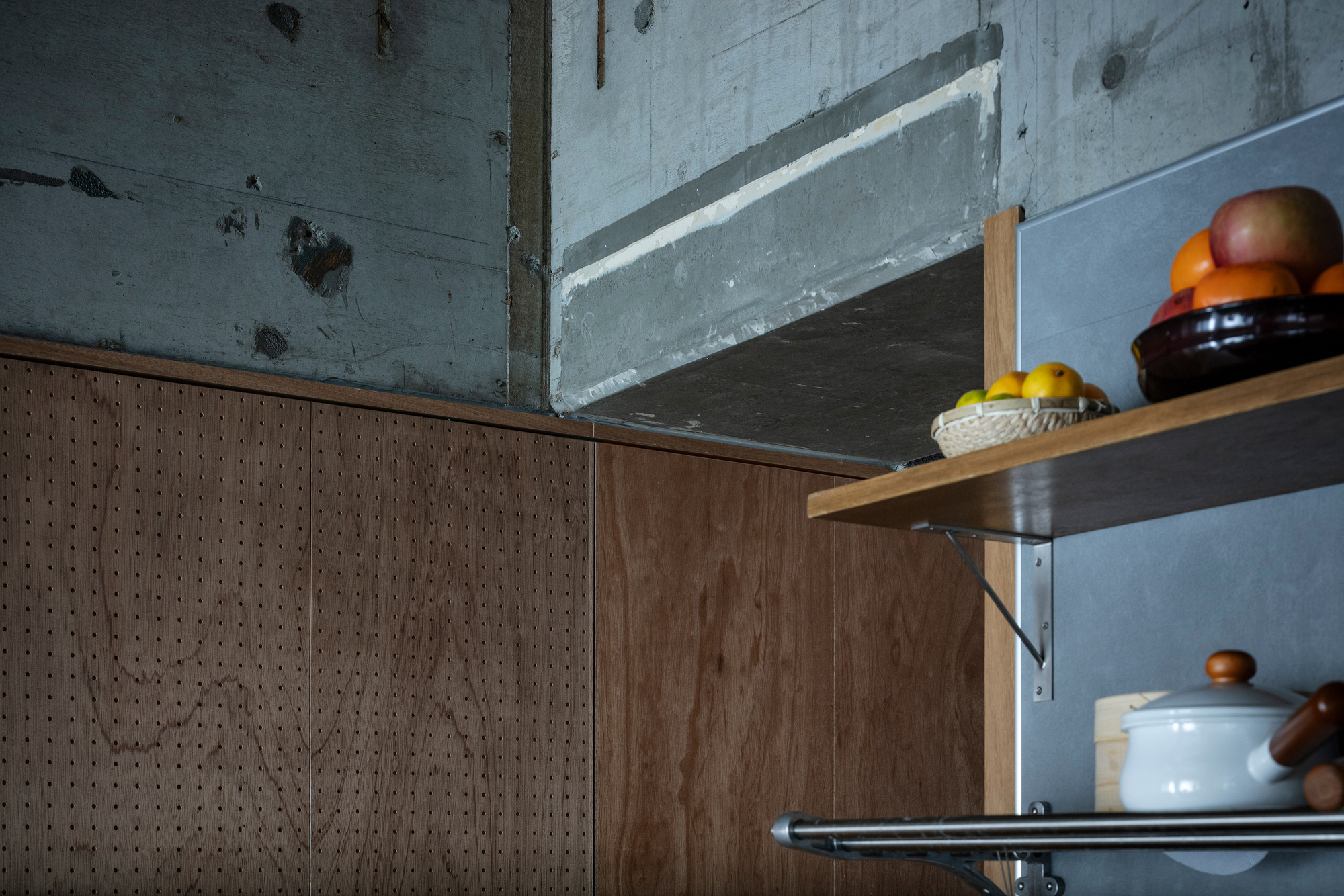 Close-up of perforated wood cabinet edge meeting steel shelves with ceramic containers beneath concrete beam