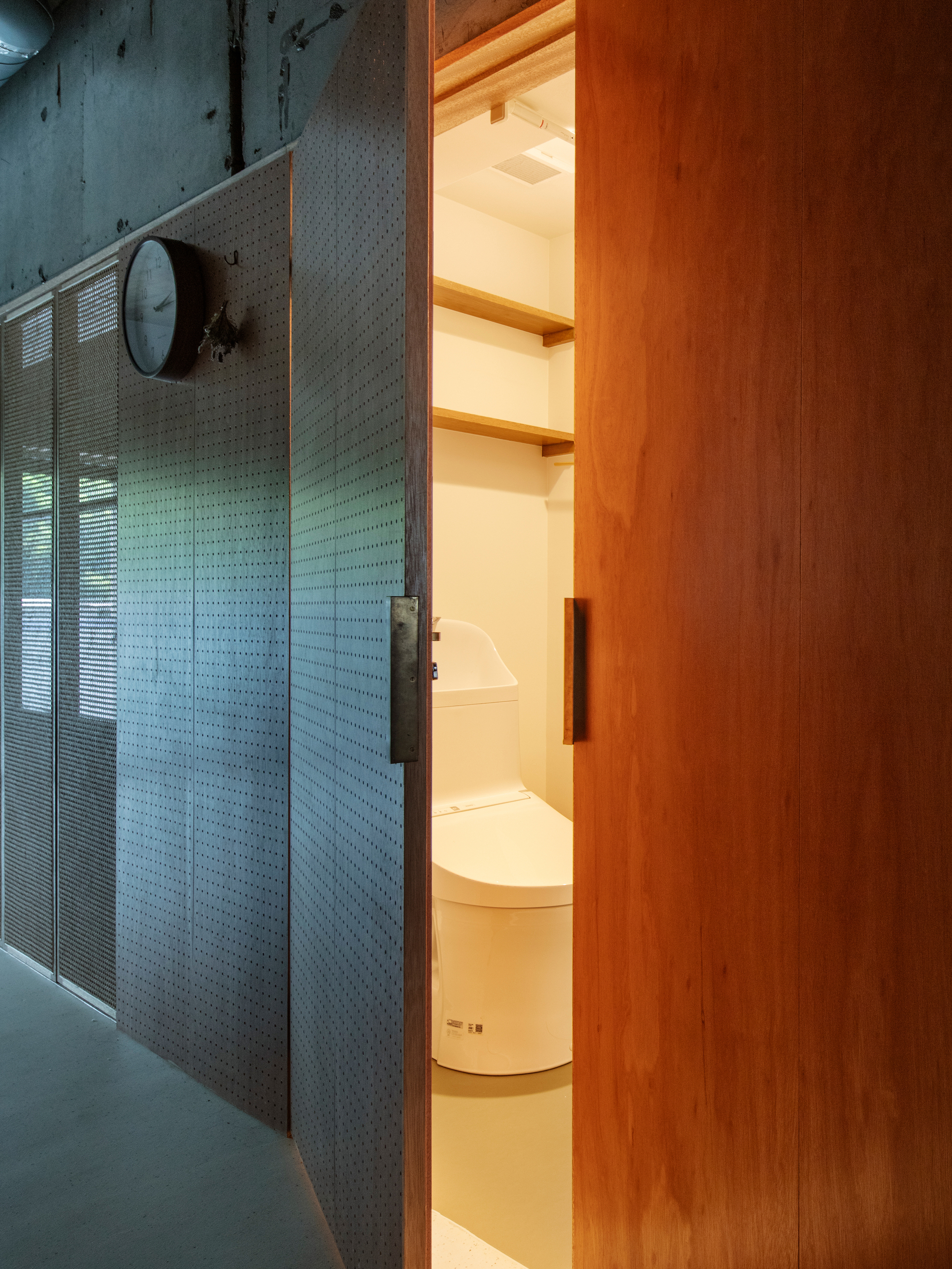 Open sliding door revealing compact bathroom with illuminated shelving and wall-mounted clock outside