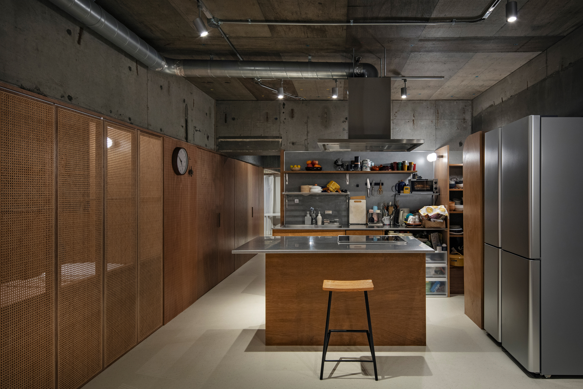 Kitchen island with stainless steel countertop, timber cabinetry and cane sliding panels against raw concrete walls