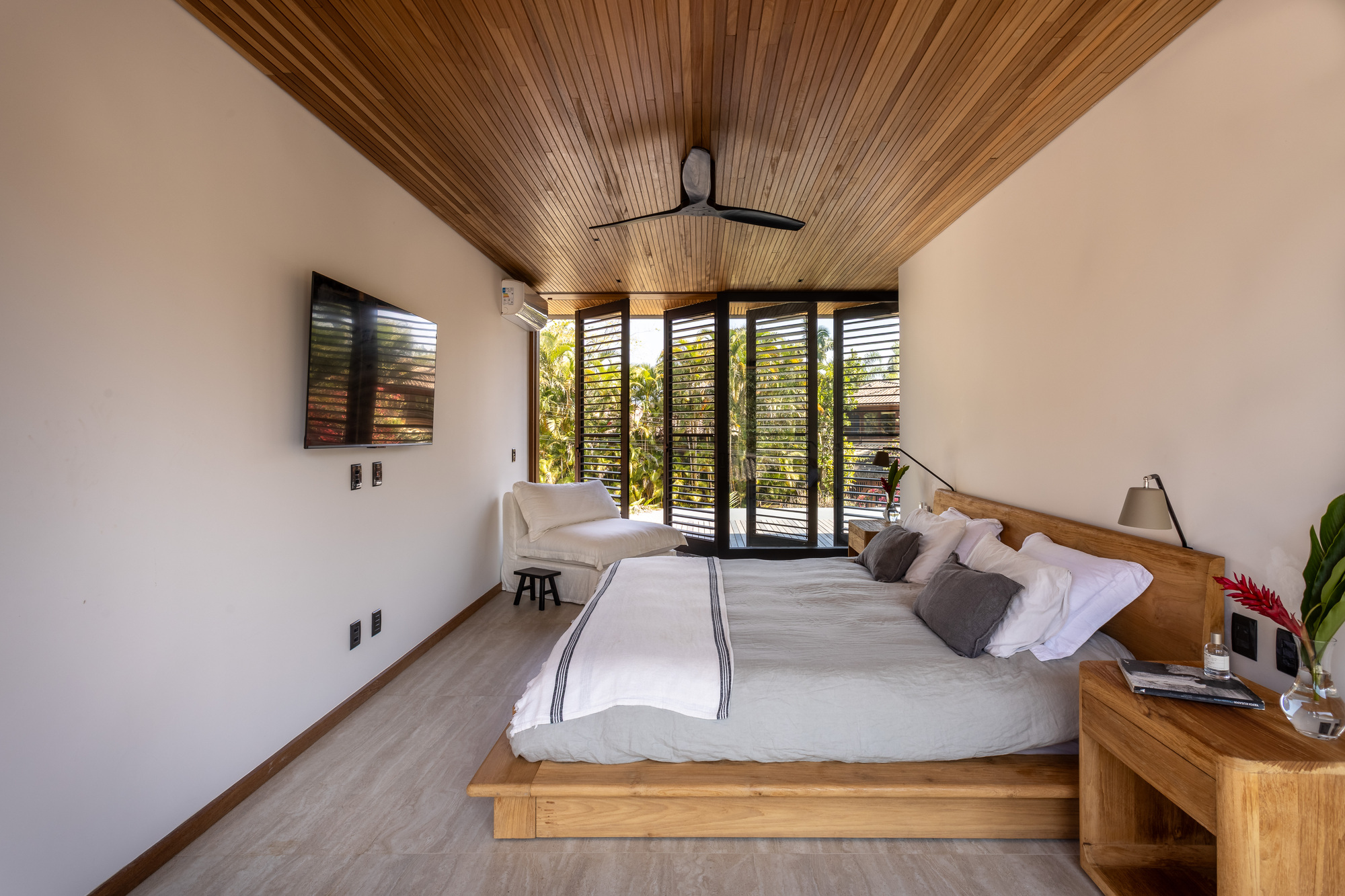 Bedroom interior with timber slat ceiling and louvered doors opening to greenery