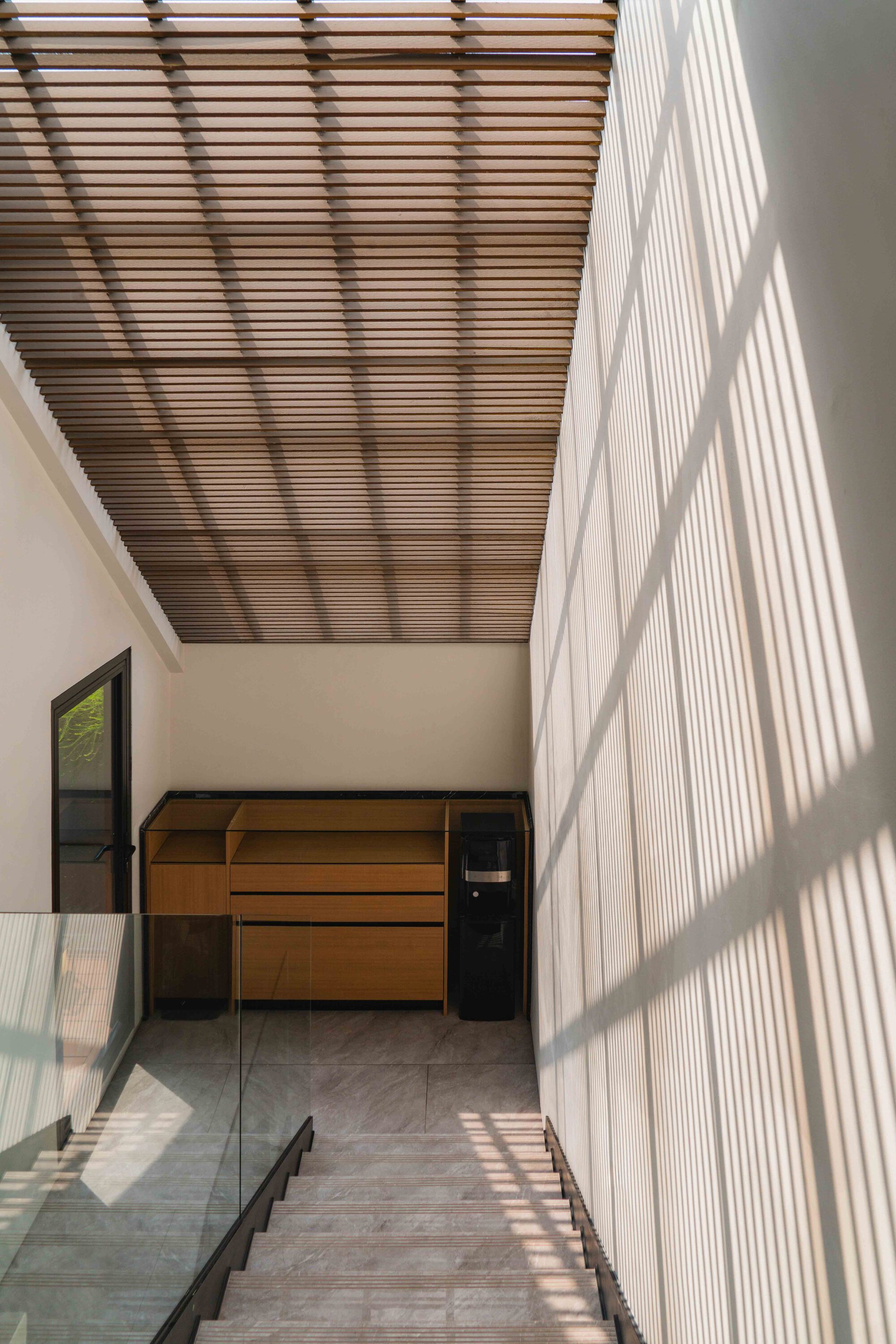 Upper hallway with slatted timber ceiling casting striped shadows across the white wall in bright daylight