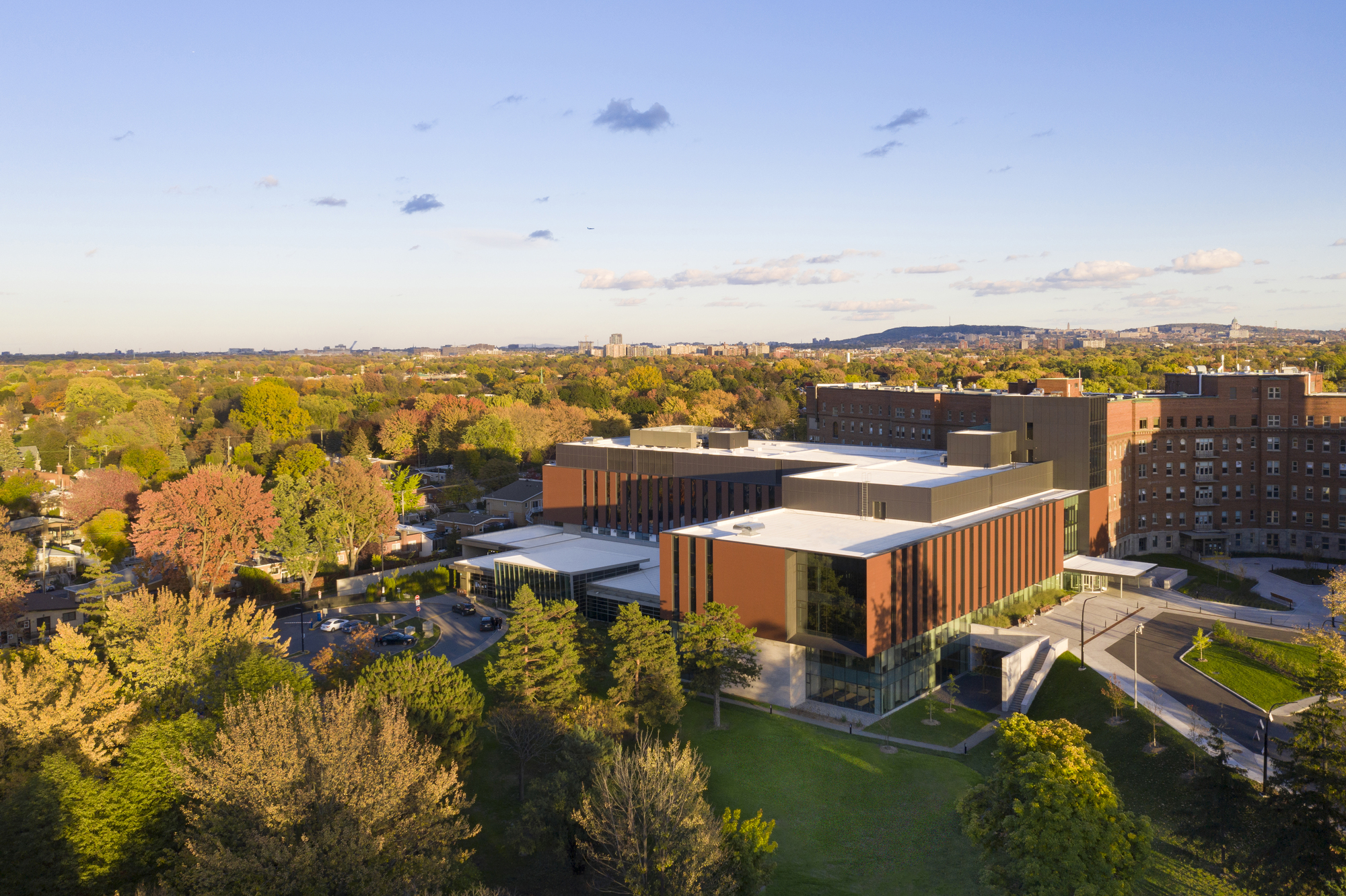 Aerial view of the complex showing multiple volumes with white roofs among autumn tree canopy