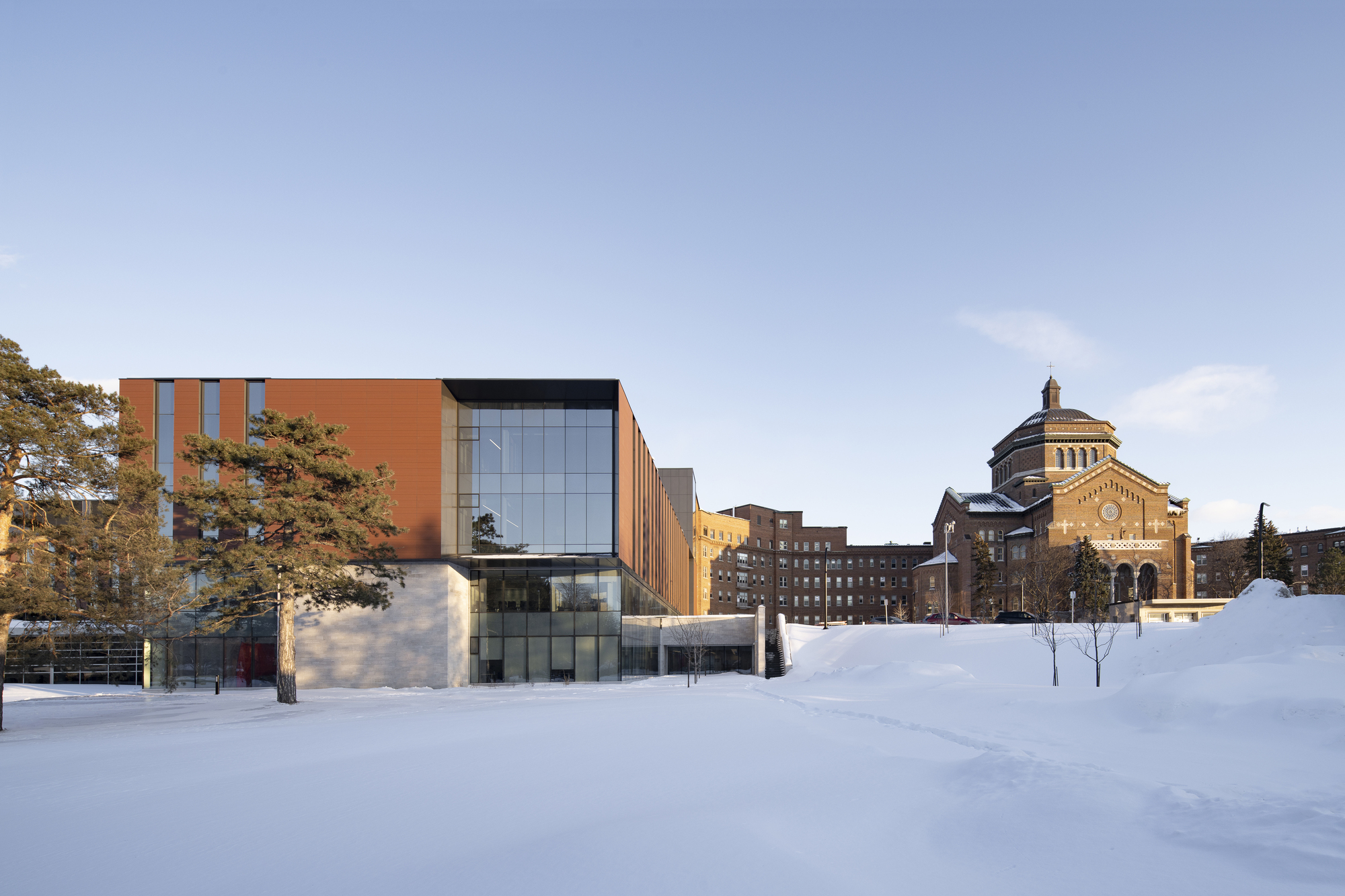 East facade of the copper-clad and glass volume across a snow-covered plaza in winter
