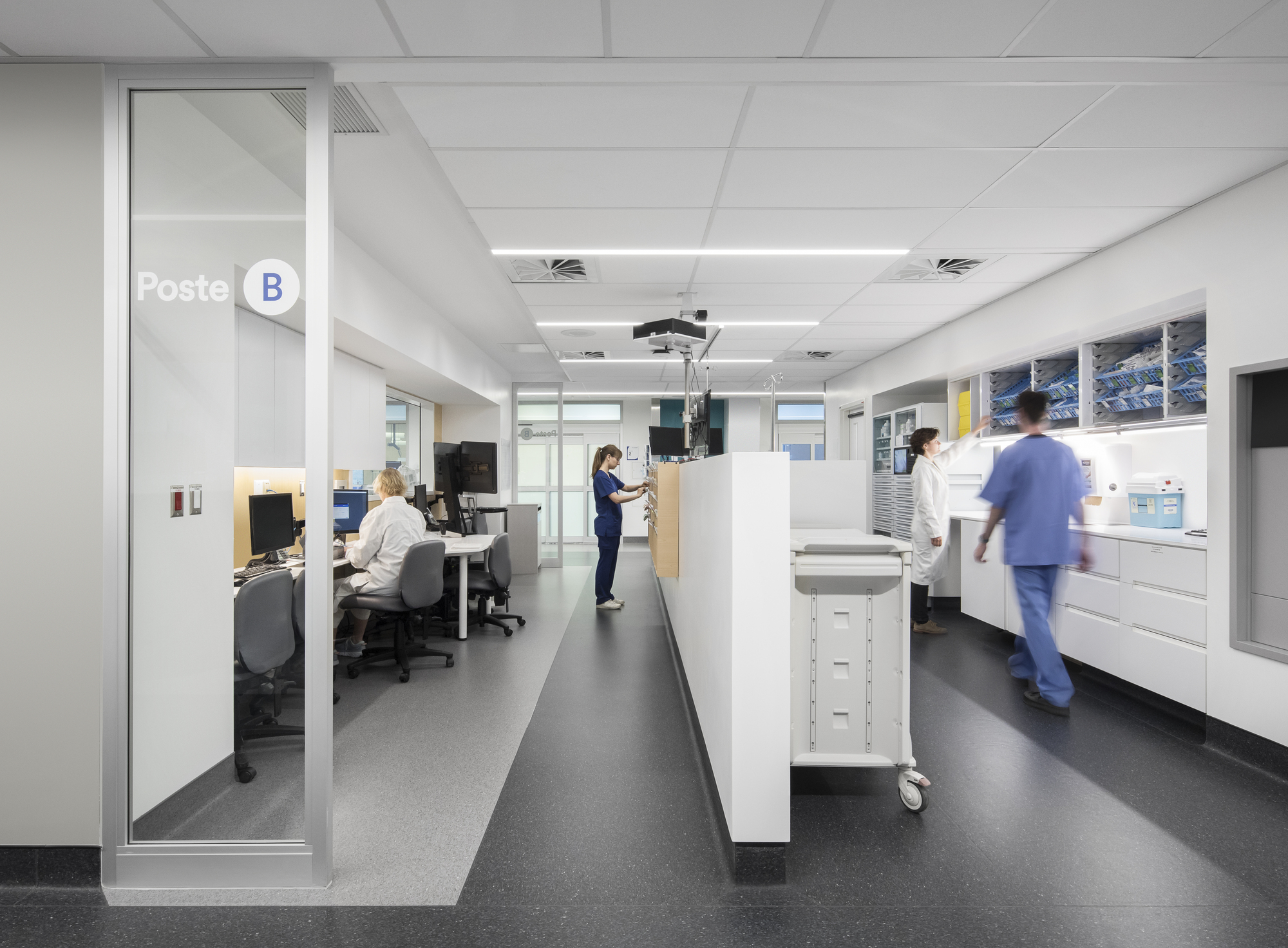 Interior workstation corridor with white casework and medical staff in motion under suspended tile ceilings