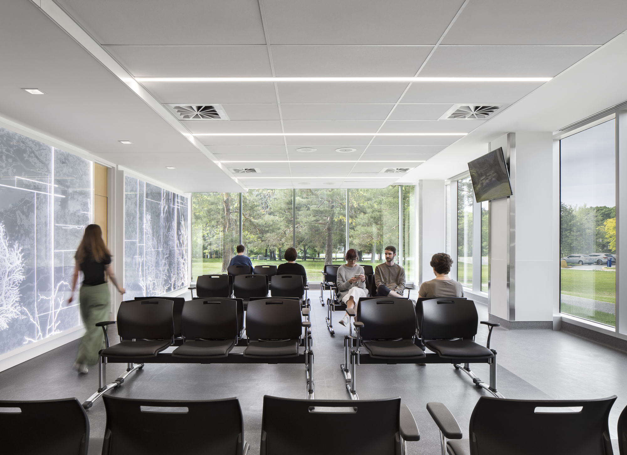 Waiting area with rows of black seating and floor-to-ceiling windows overlooking green landscape