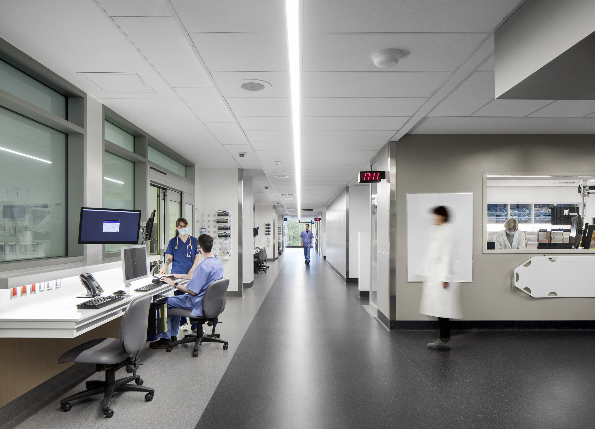 Corridor view with reception desks along one side and medical staff moving through white-walled spaces