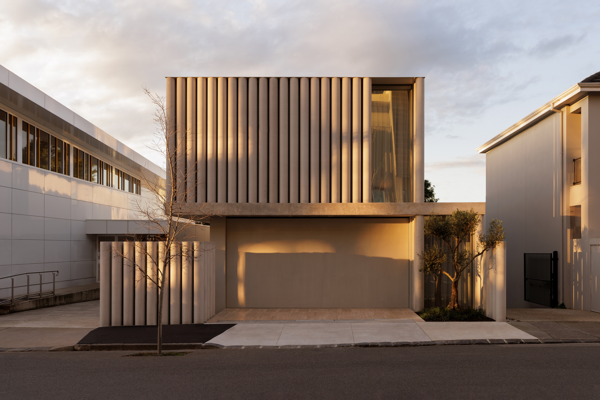 Street facade with vertical timber screening over garage and cantilevered upper volume at dusk