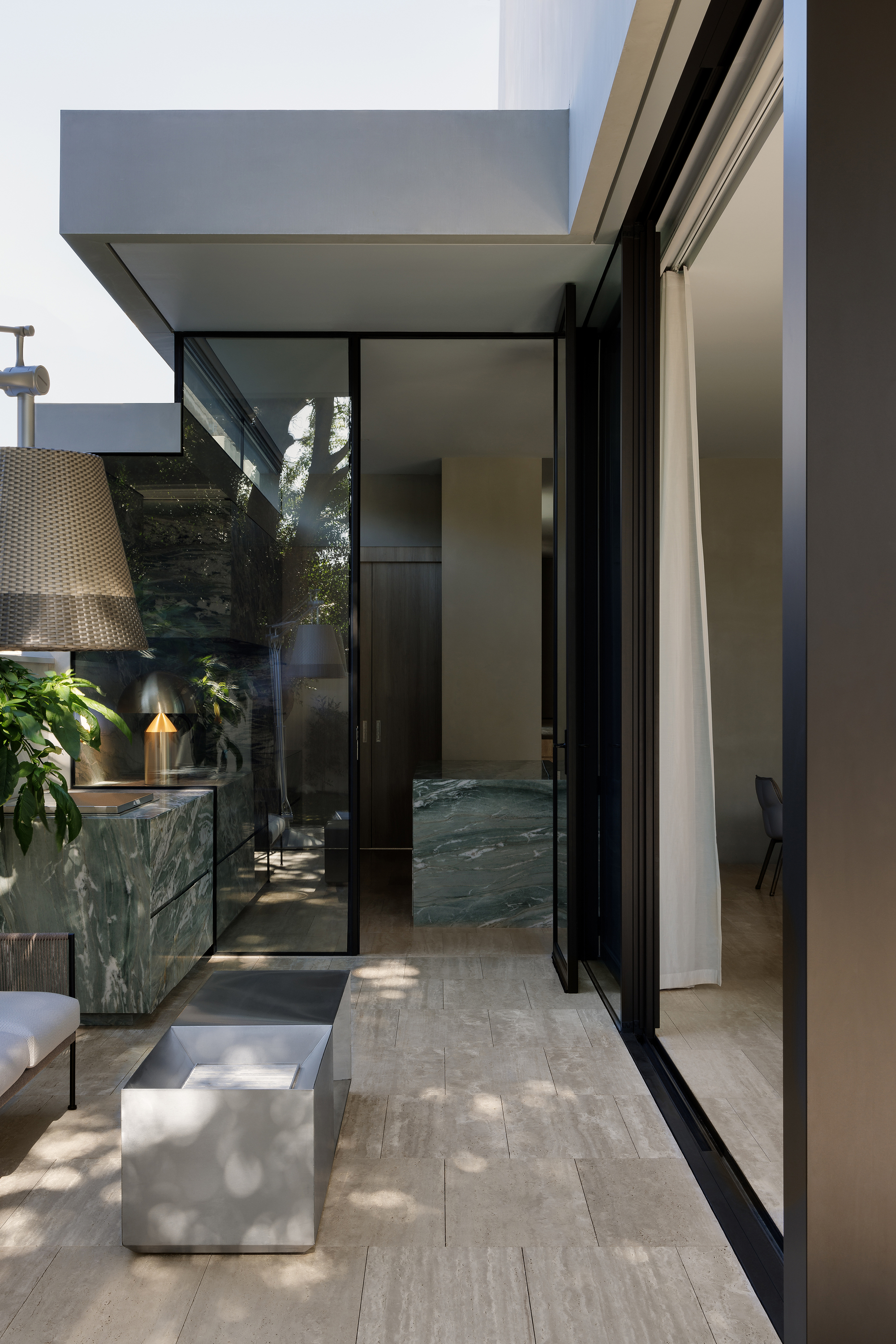 Sliding glass doors opening from the interior to a sheltered courtyard with dappled sunlight