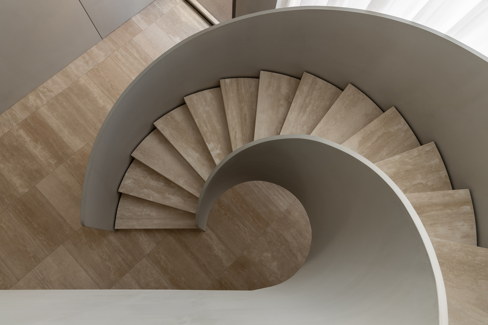 Top-down view of spiral staircase with travertine treads and curved white balustrade