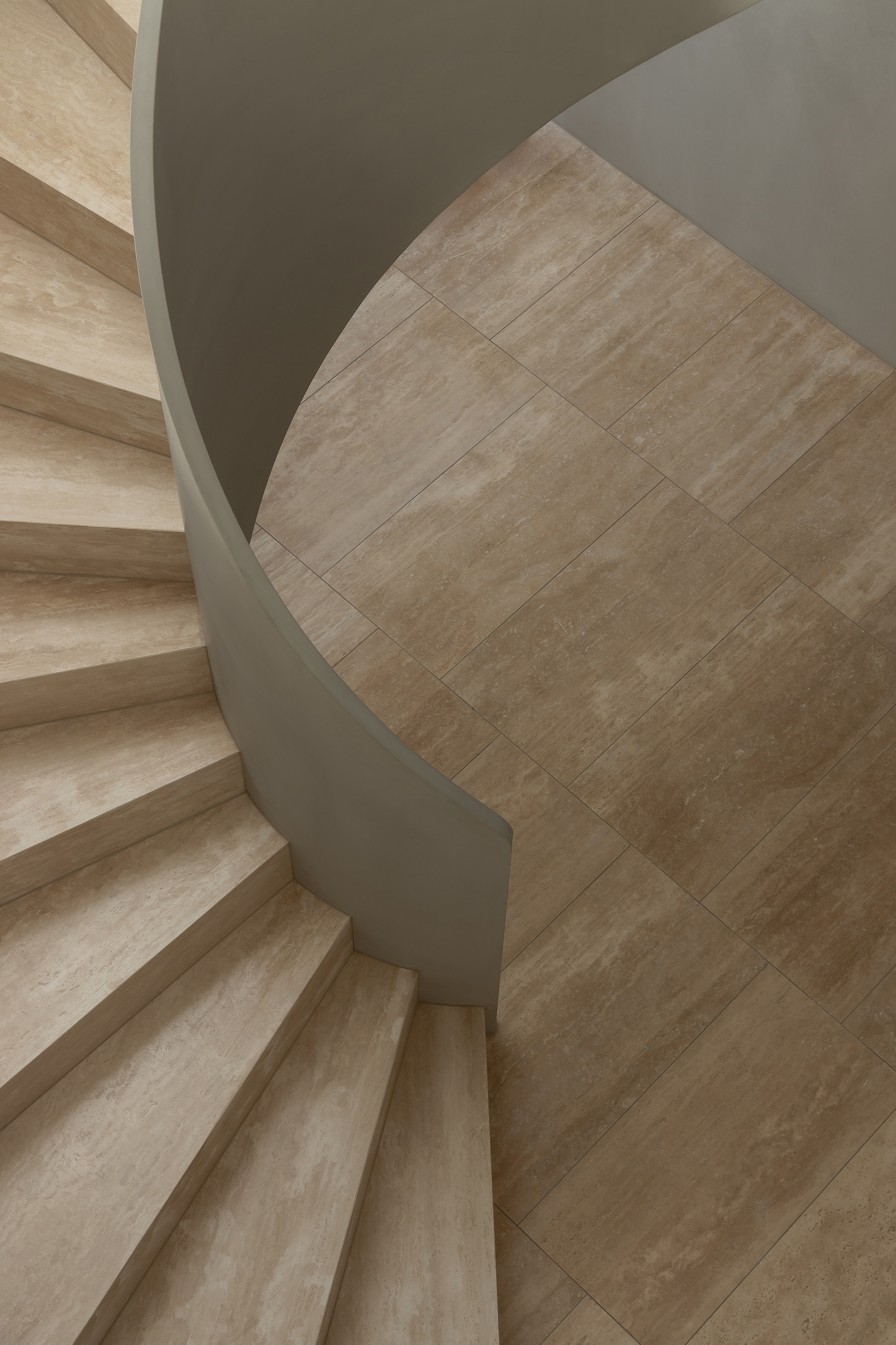 Upward view of spiral staircase showing travertine steps and curved taupe-painted stringer