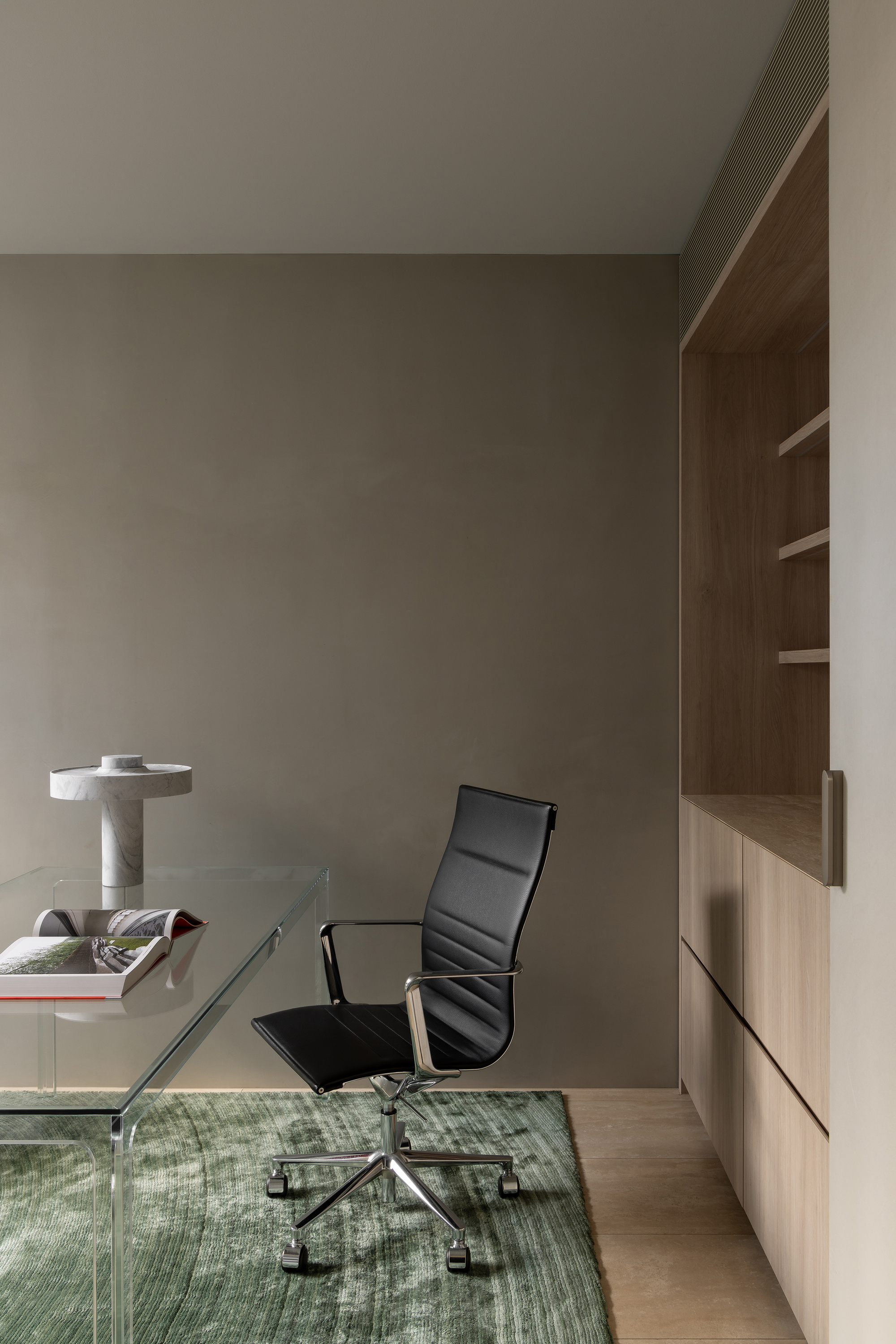 Home office with glass desk, black leather chair, and timber built-in shelving on green rug