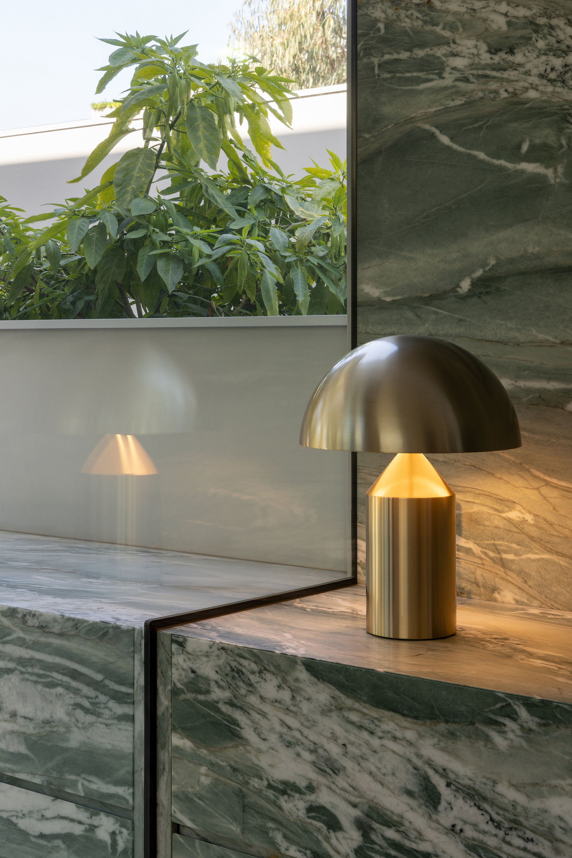 Brass dome table lamps on a marble counter beside glazing overlooking foliage in daylight