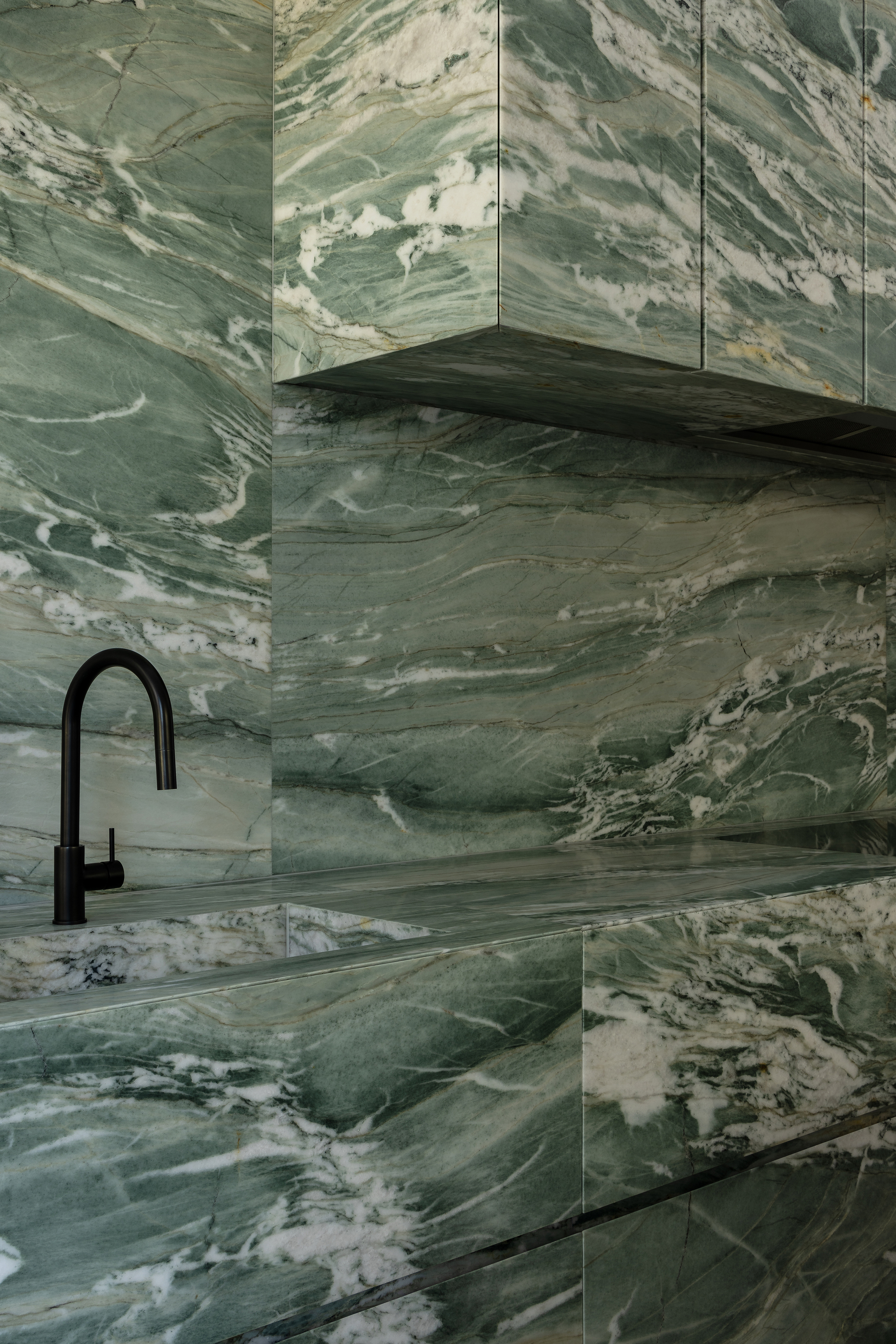 Black gooseneck tap against green and white swirled marble walls and countertop in close-up