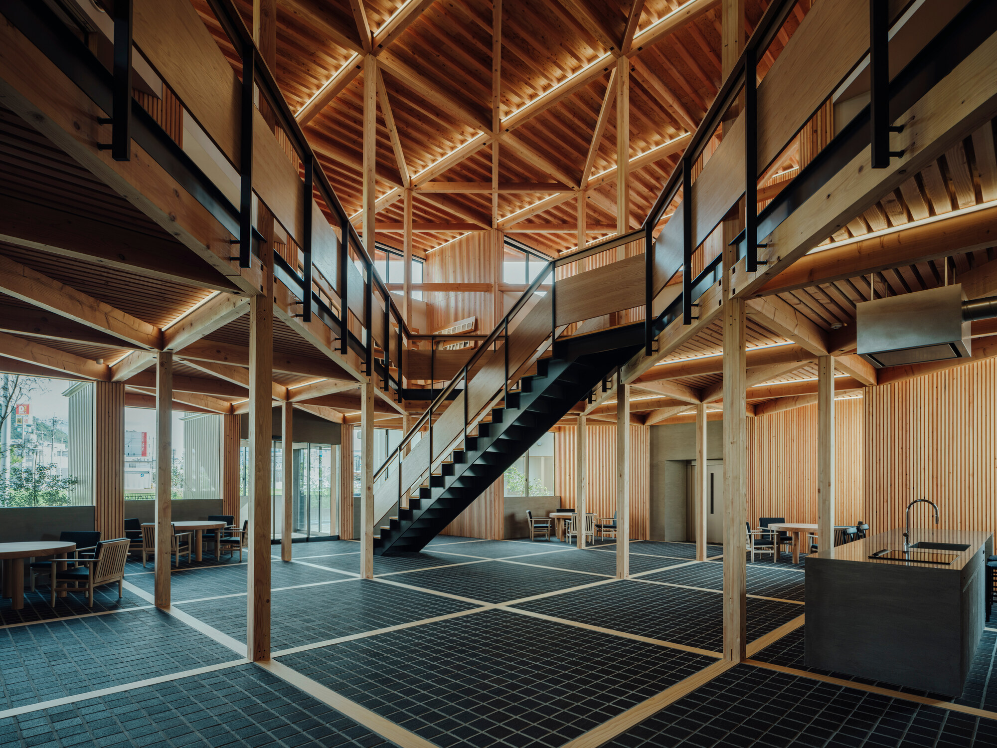 Double-height interior with exposed timber frame, black steel staircase and green tile flooring