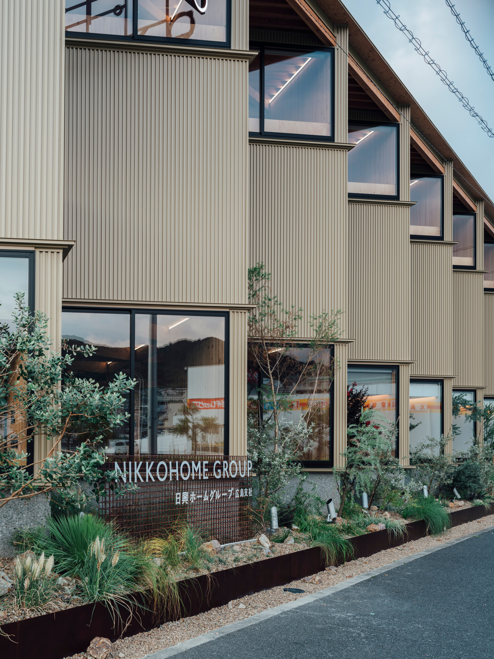 Corner detail showing vertical ribbed cladding and planted beds with ornamental grasses at dusk