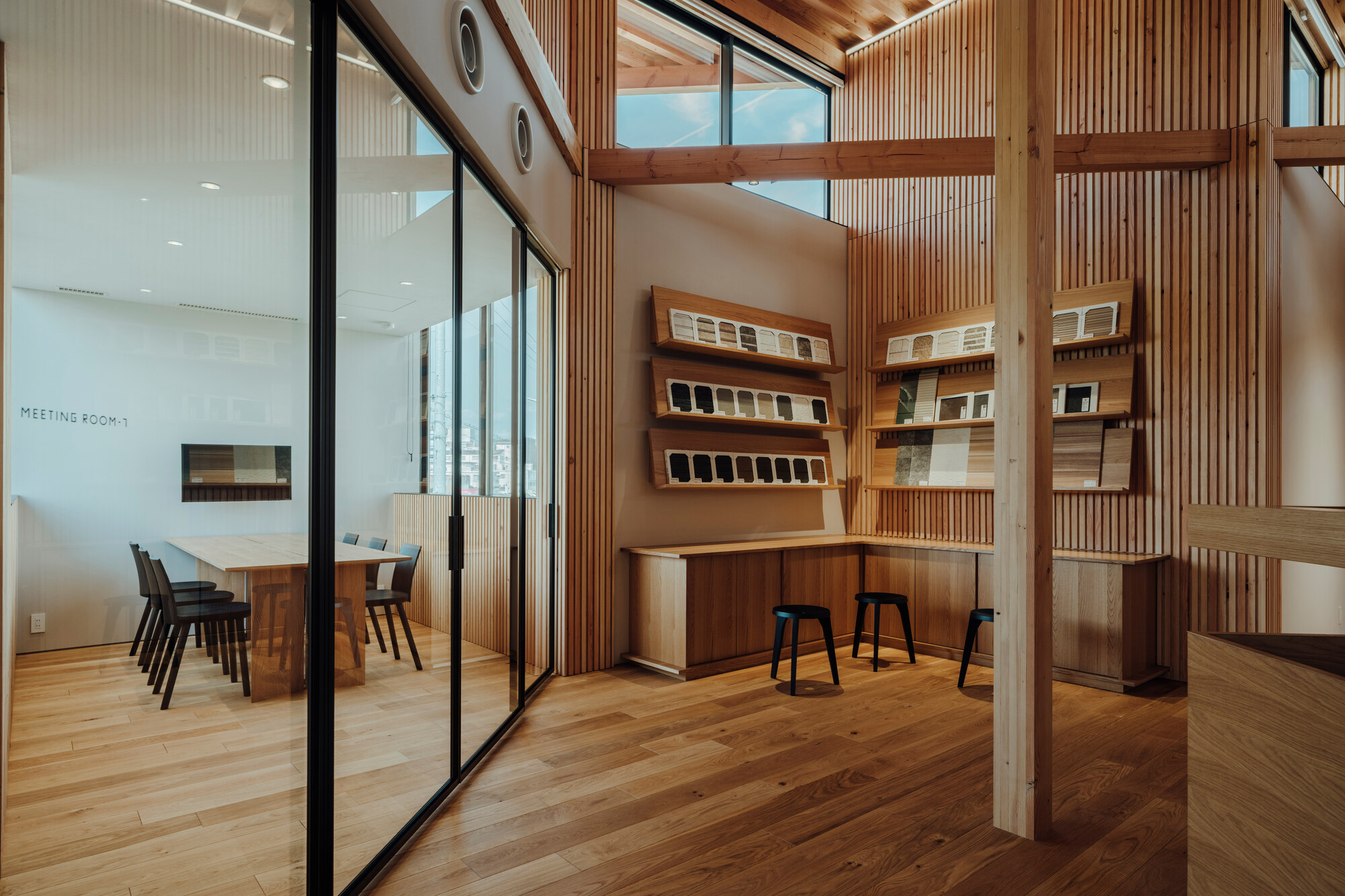 Reception area with timber post and beam structure and wall-mounted material samples beside glazed meeting room