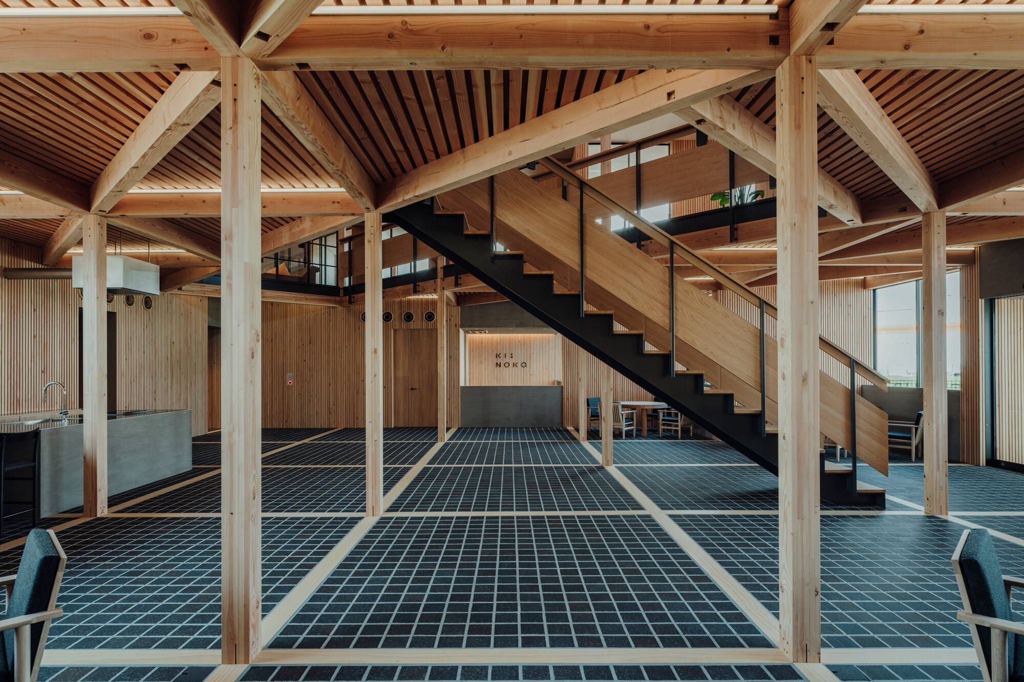 Open interior showing exposed timber frame with blue grid floor tiles and steel staircase to mezzanine
