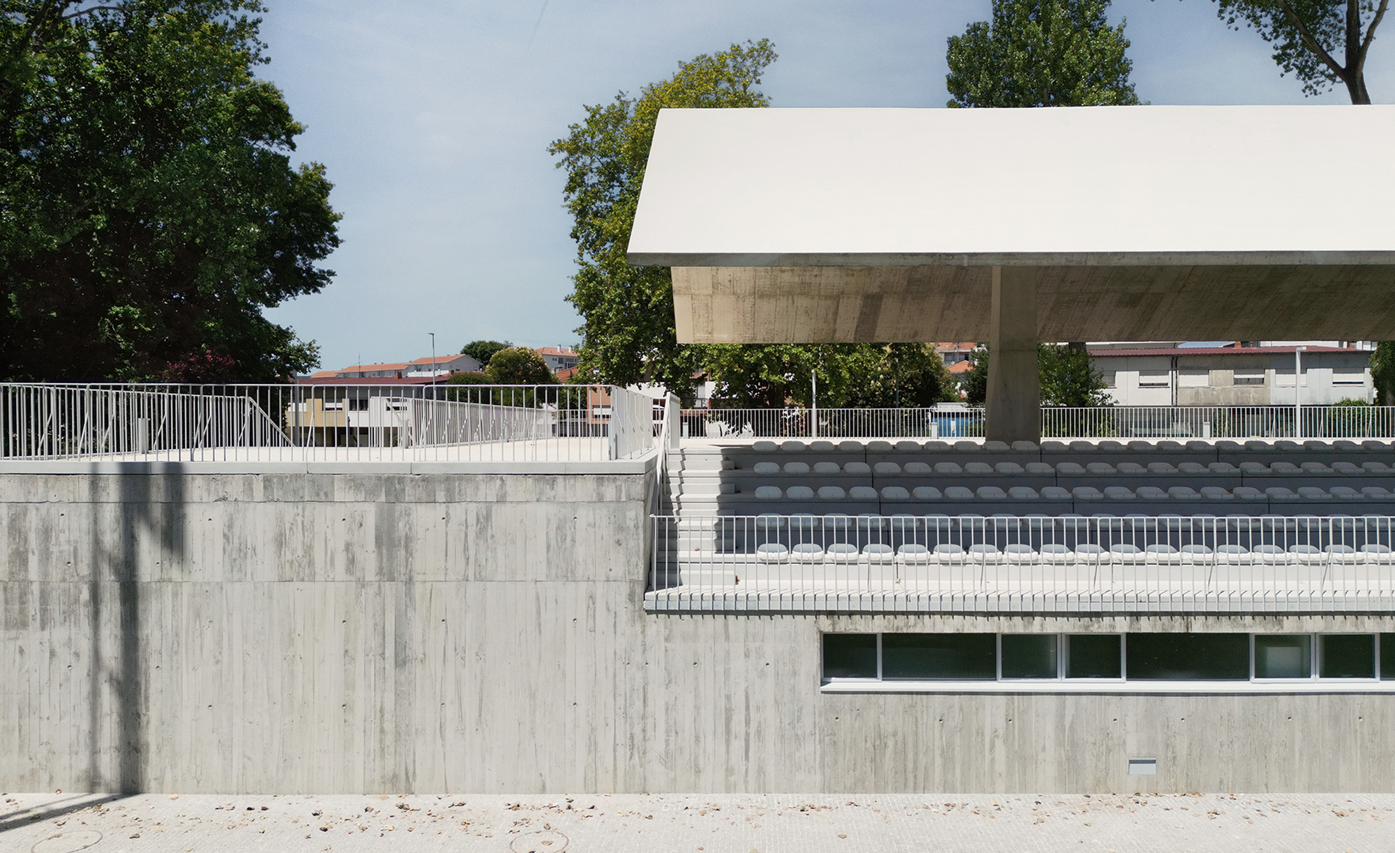 Board-marked concrete retaining walls and stadium seating tiers beneath the overhanging canopy structure