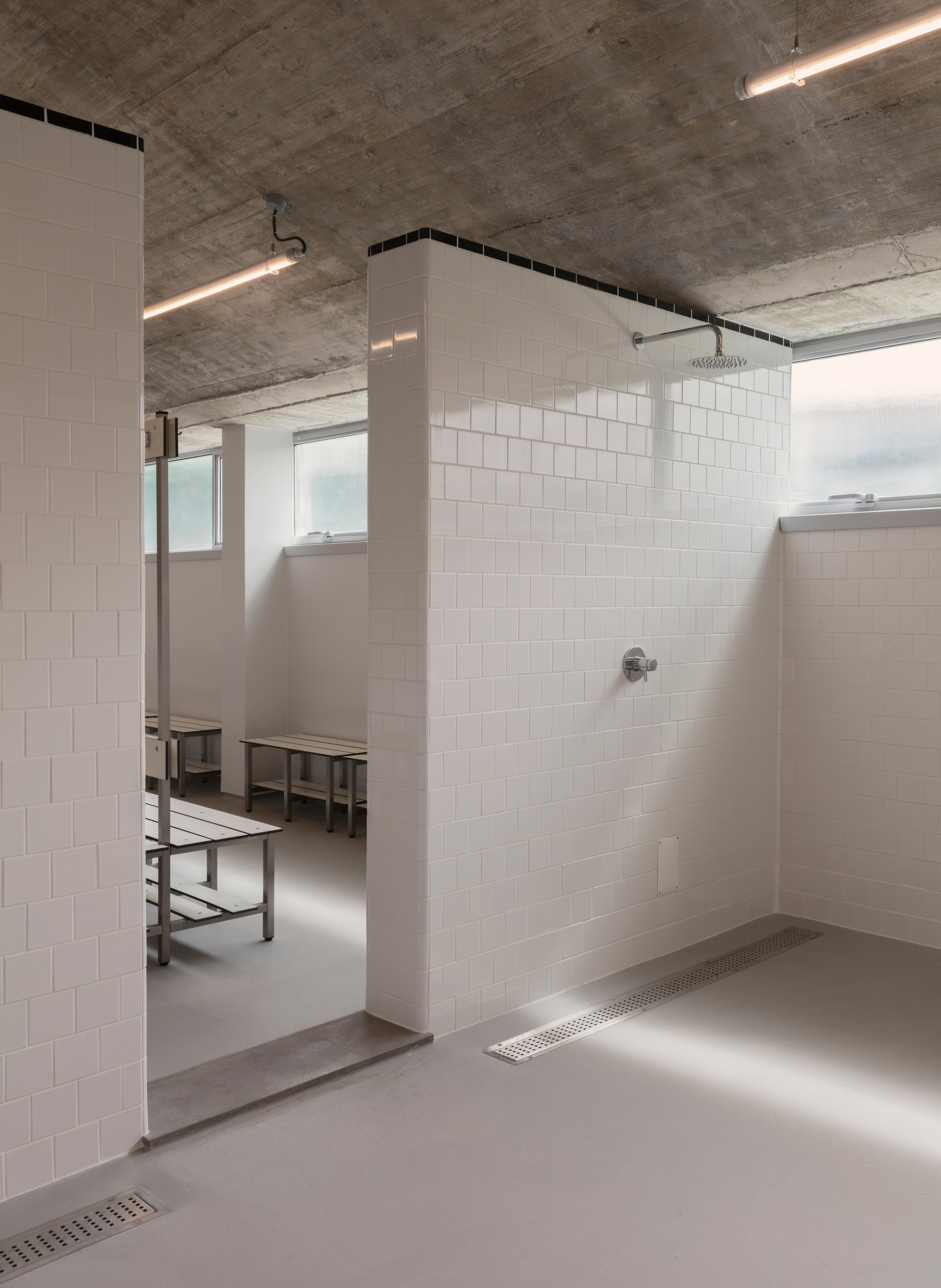 Shower enclosure with white subway tiles under an exposed concrete soffit and linear lighting