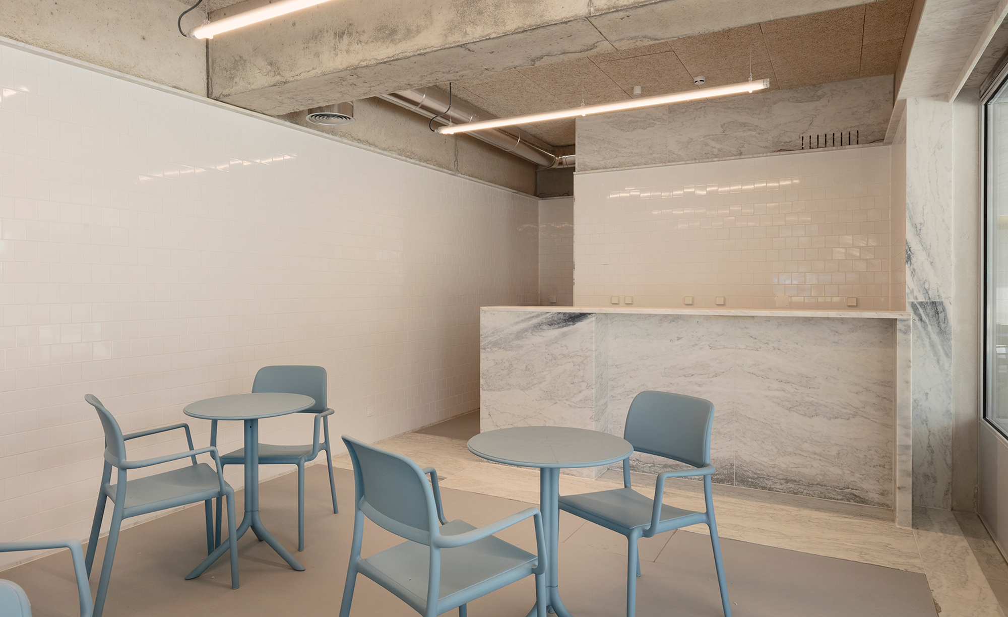 Waiting area with blue chairs and veined marble reception counter under an exposed concrete ceiling