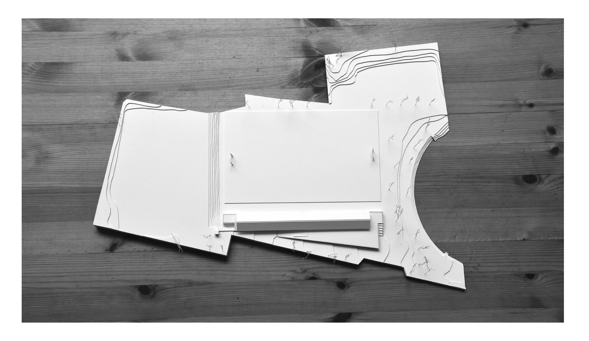 Photograph of layered cardboard study models with contour lines on a wooden surface