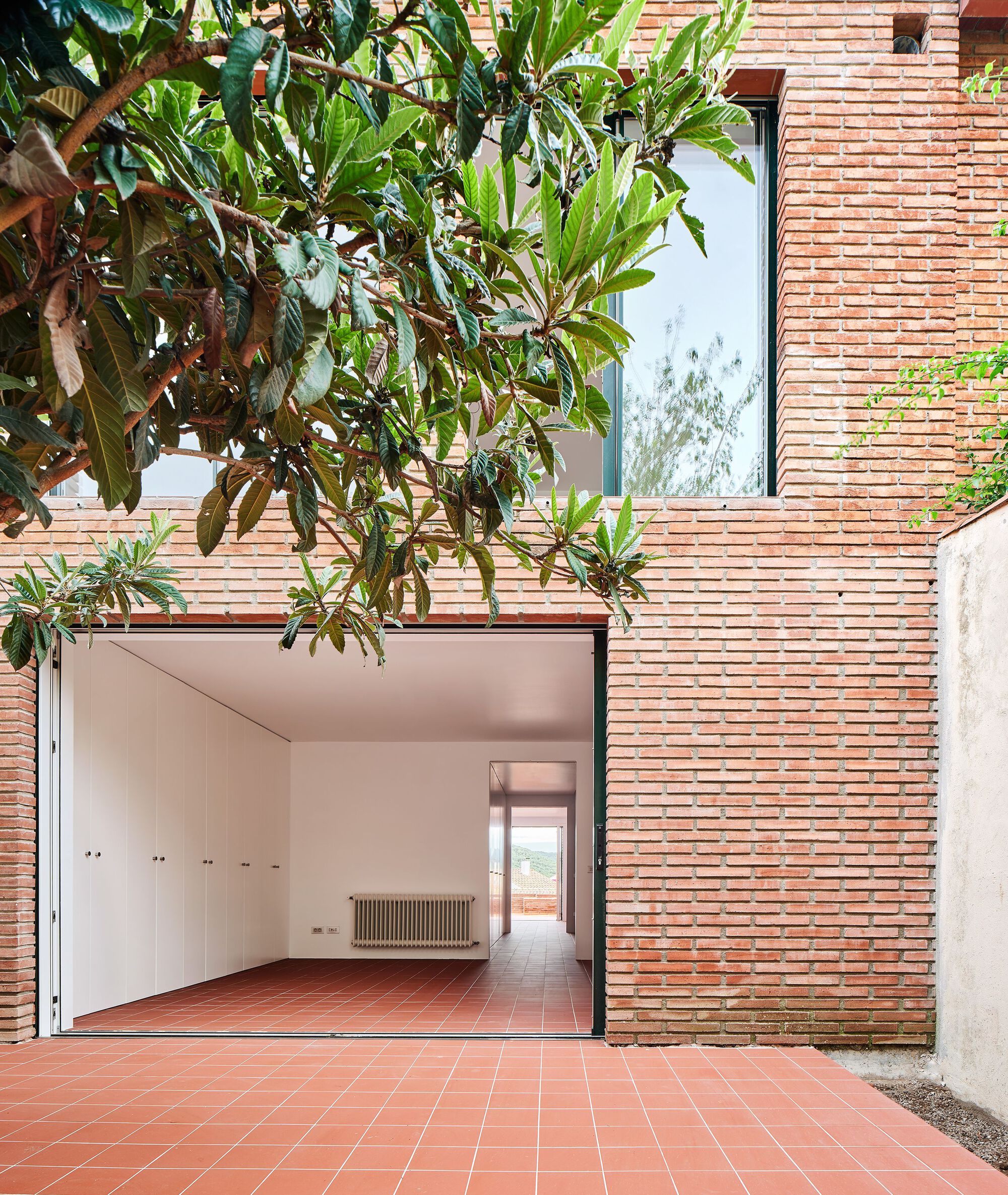 Terracotta tile courtyard with horizontal brick facade and planted frangipani tree overhead