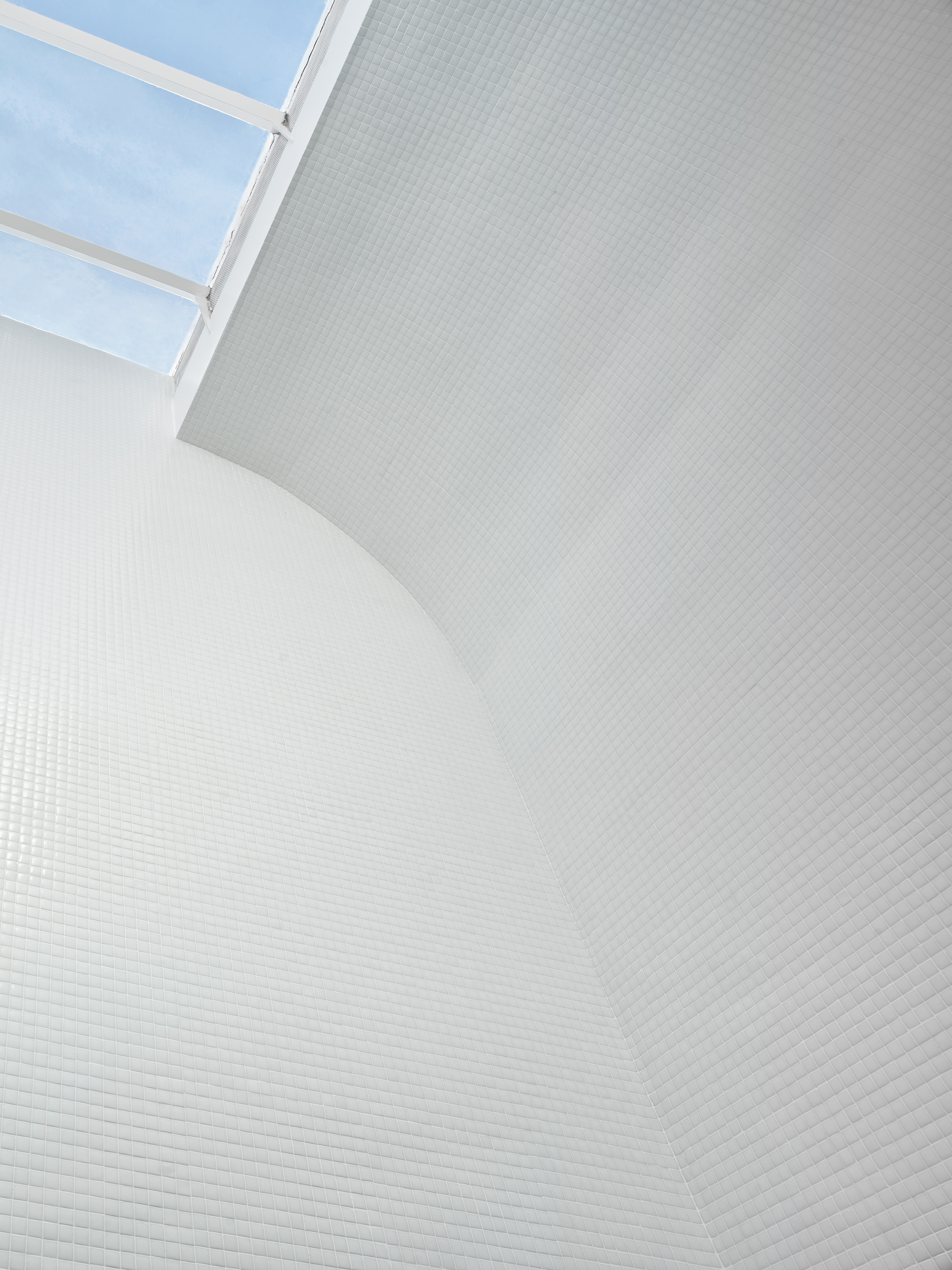 Curved white mosaic tile wall rising to a skylight under blue sky