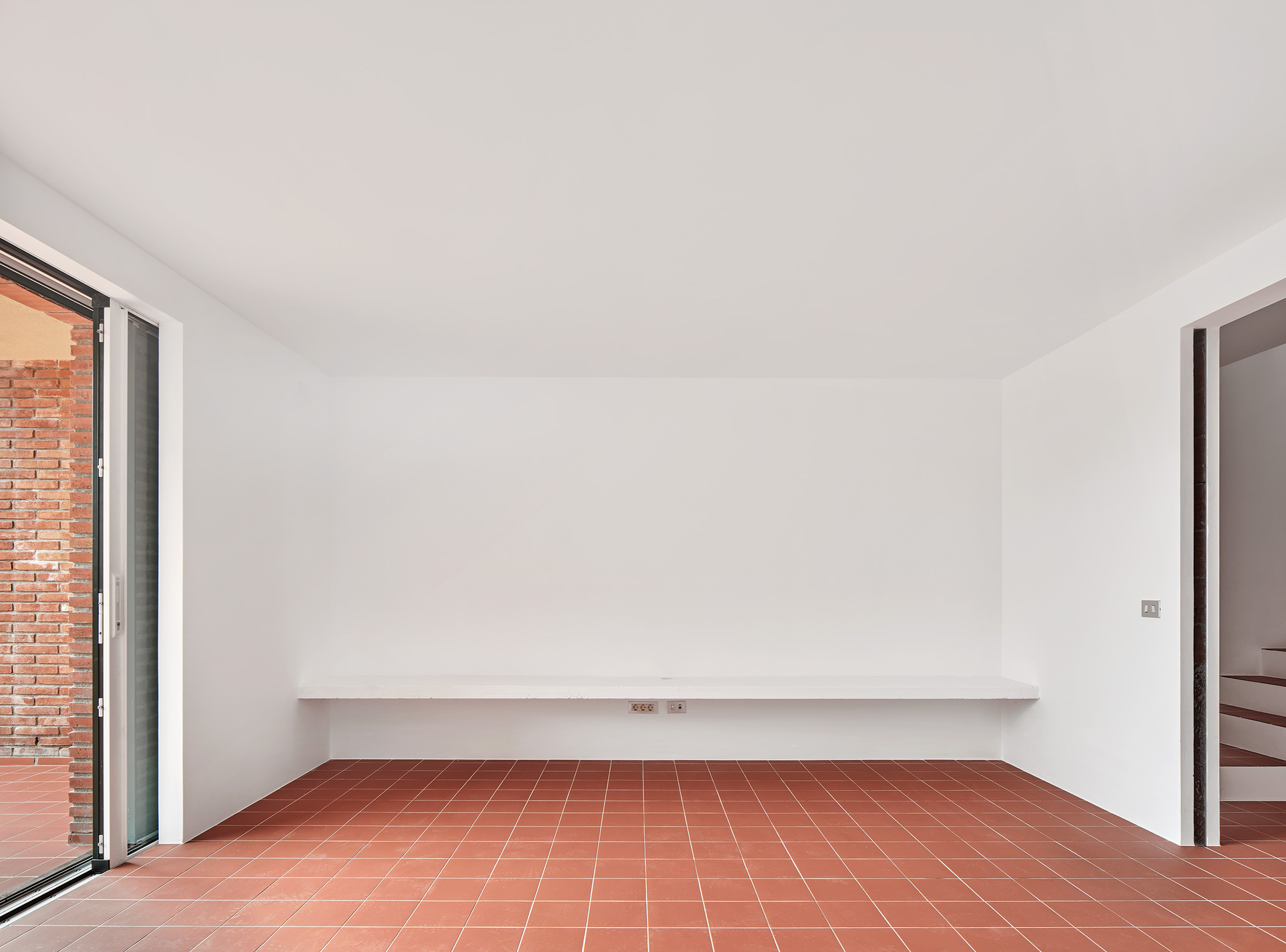 Empty room with terracotta tile floor and continuous white ledge beneath plastered walls