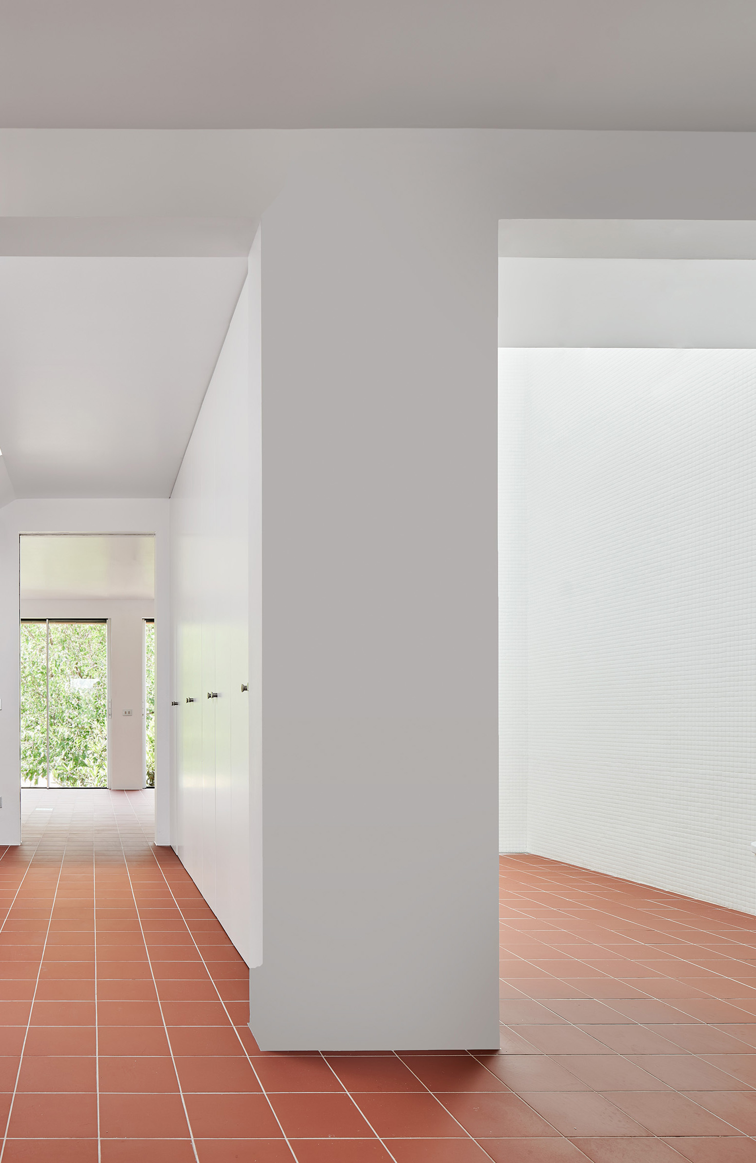 Terracotta tiled hallway framed by white plastered walls with view through to garden beyond